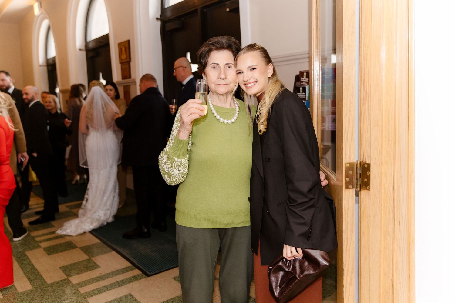 Older woman in green outfit and young woman in black posing at wedding.