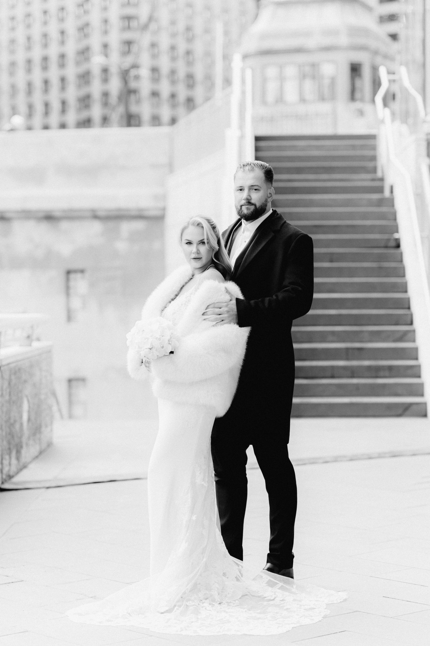 Black and white photo of elegant bride and groom posing on city steps.