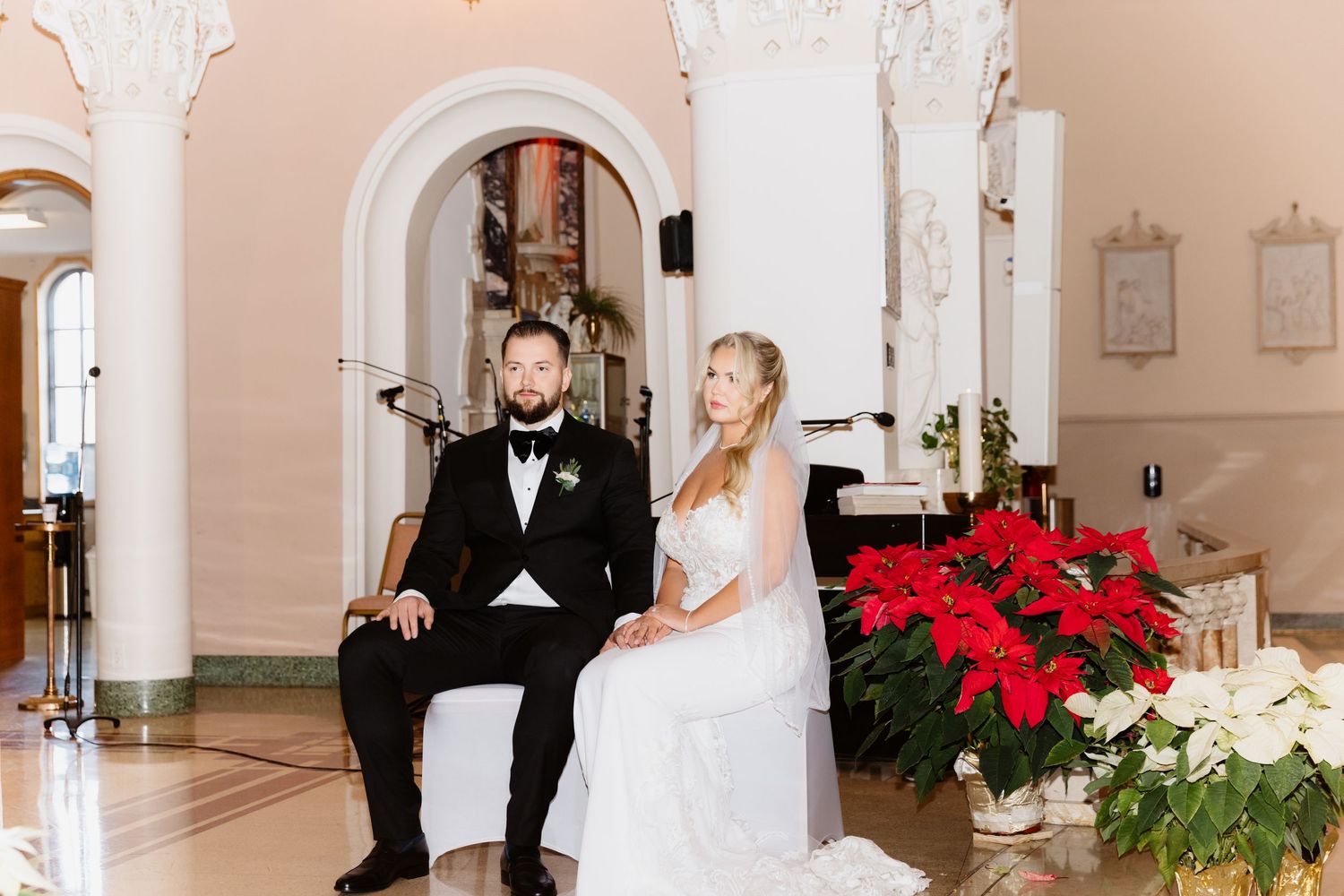 Bride and groom seated at church altar with red poinsettias during Christmas wedding ceremony.
