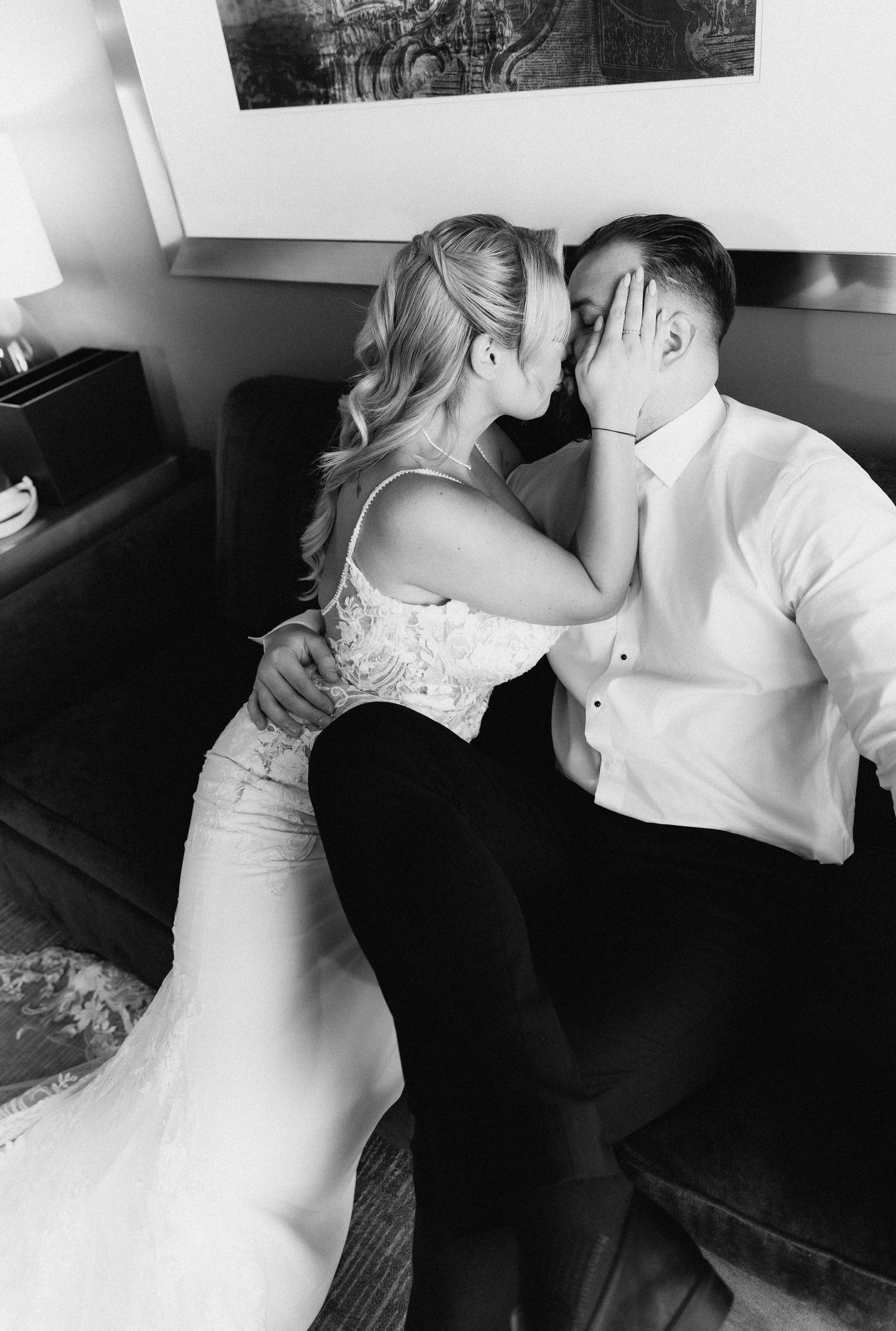 Bride in lace gown tenderly holds grooms face for a kiss in black and white portrait.
