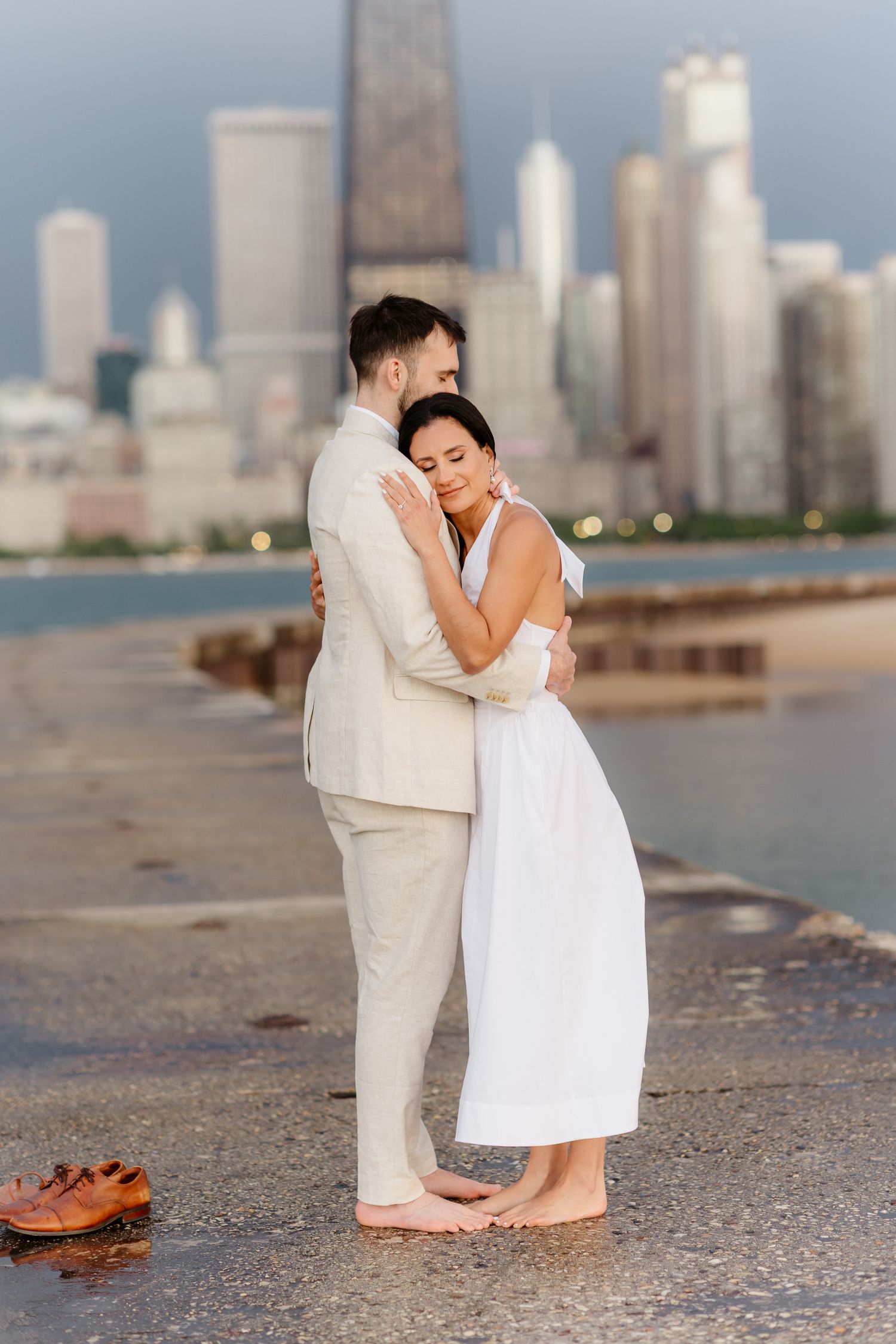 Barefoot couple embraces on Chicago lakefront pier at sunset with shoes resting on wet concrete nearby.