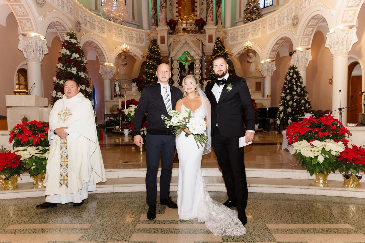 Bride and groom posing with officiant in a beautifully decorated Christmas church, surrounded by poinsettias and Christmas trees.