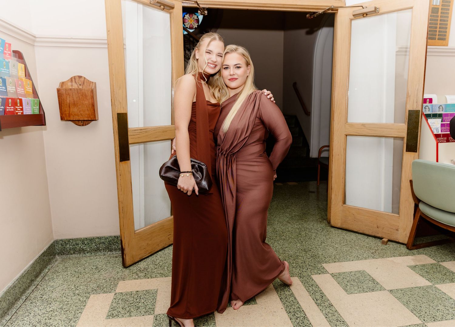 Two smiling women in brown formal gowns posing together at elegant event.