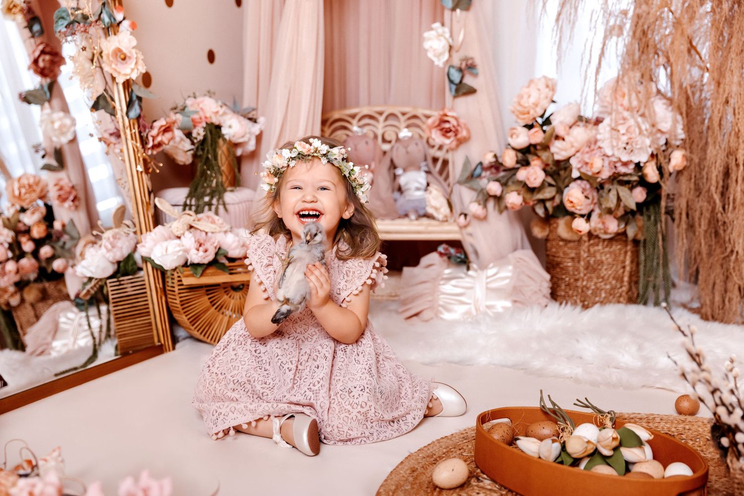 Joyful little girl in pink floral dress and flower crown laughing among roses and Easter decorations.