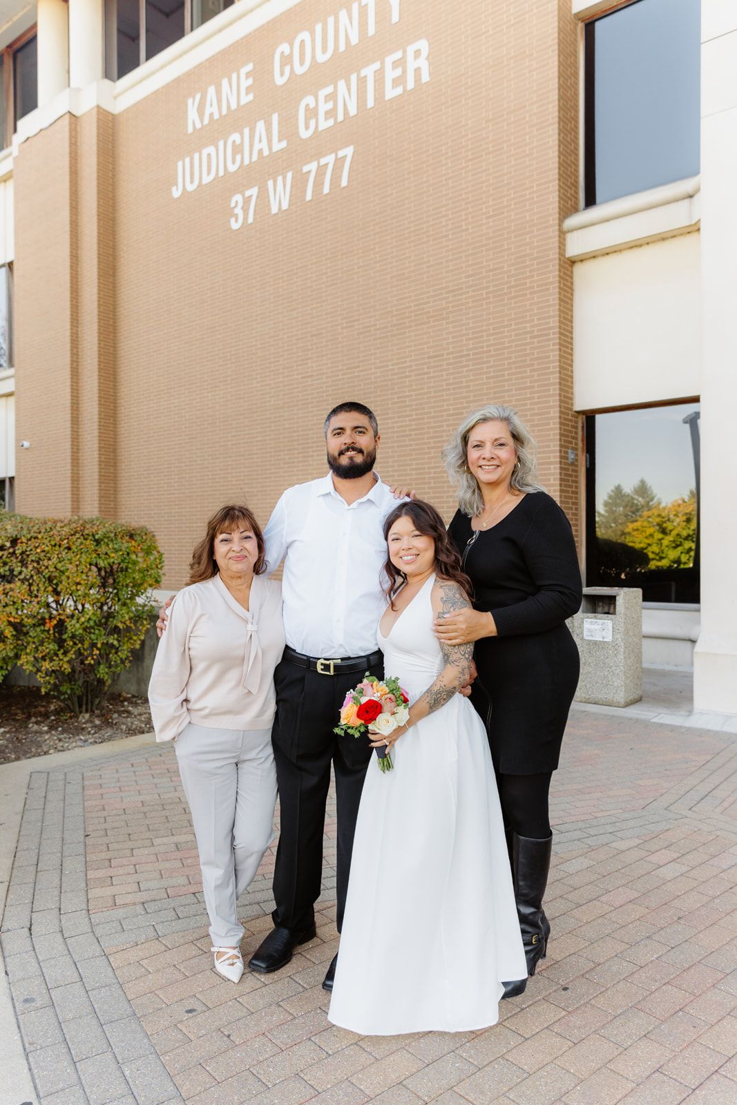Wedding couple posing with two family members outside Kane County Judicial Center after courthouse marriage.