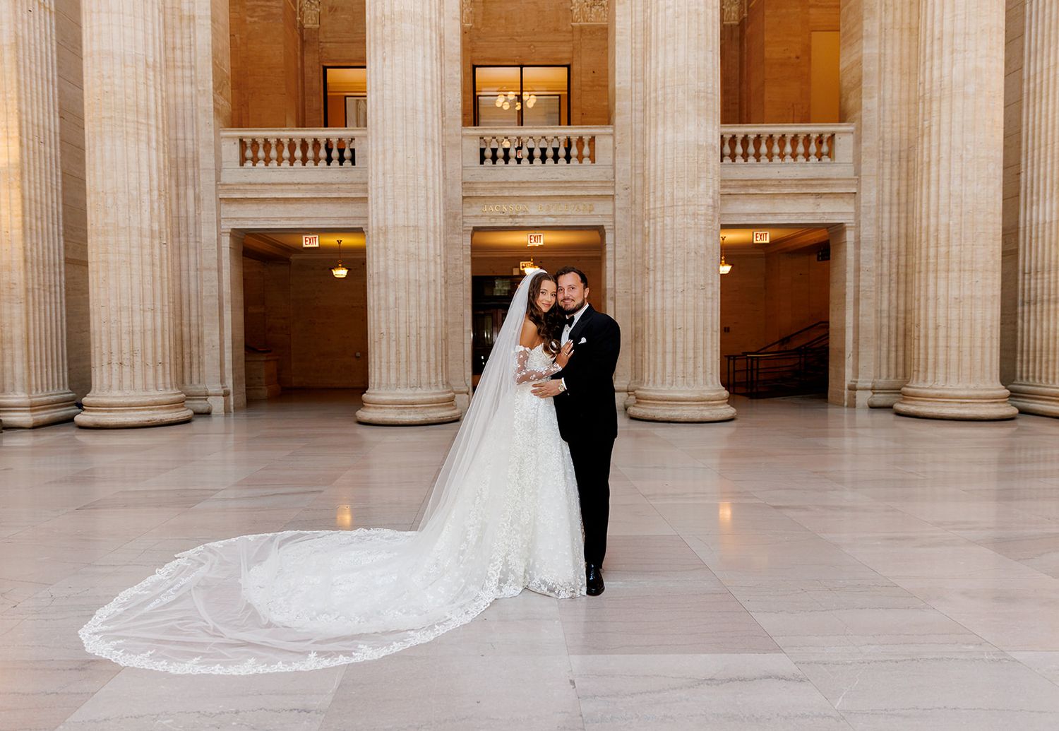 Bride and groom embrace among grand columns in stunning marble wedding venue hall.