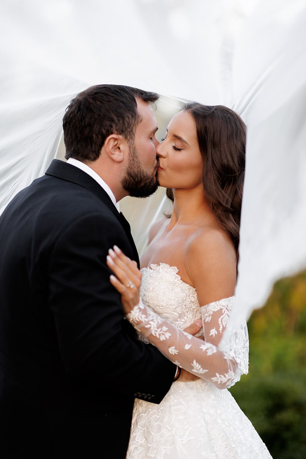 A bride and groom share a romantic kiss under a flowing white veil on their wedding day.