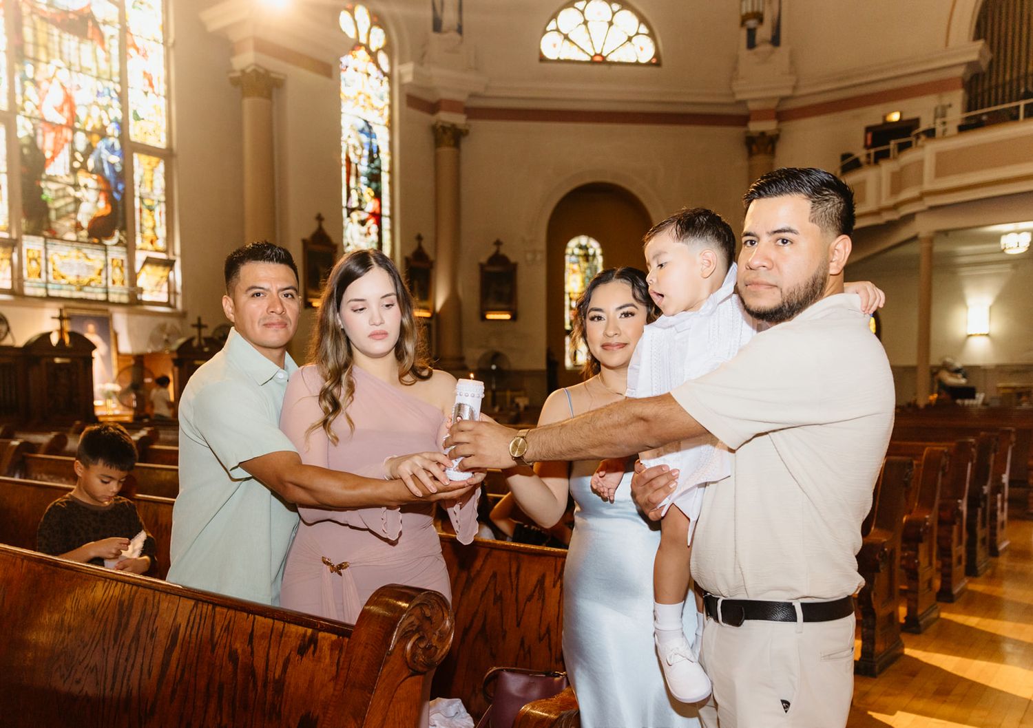 Family posing together in an ornate church holding a candle during a baptism ceremony.