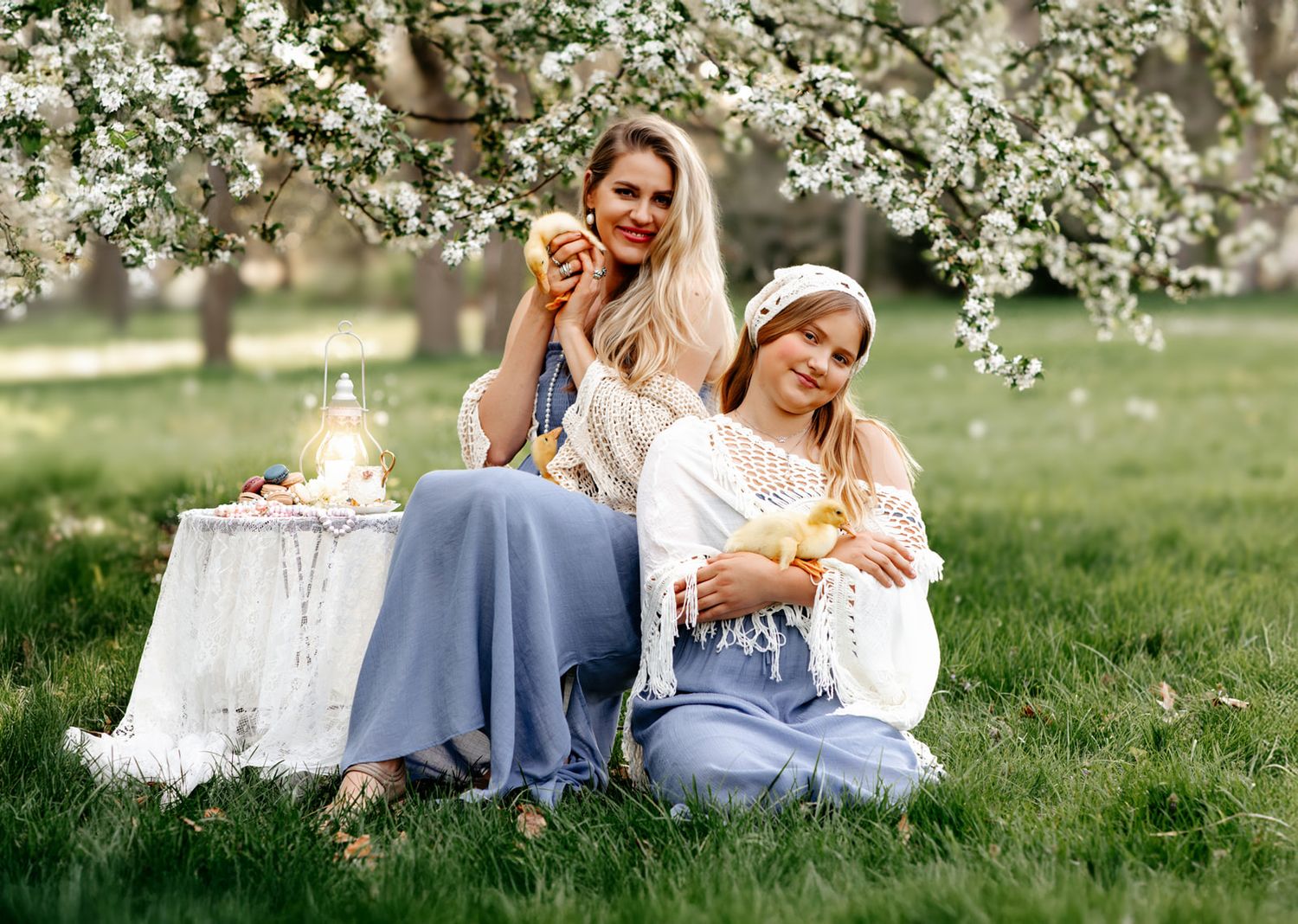 Two women enjoying a spring picnic under blooming trees, holding fruit and smiling in blue skirts.