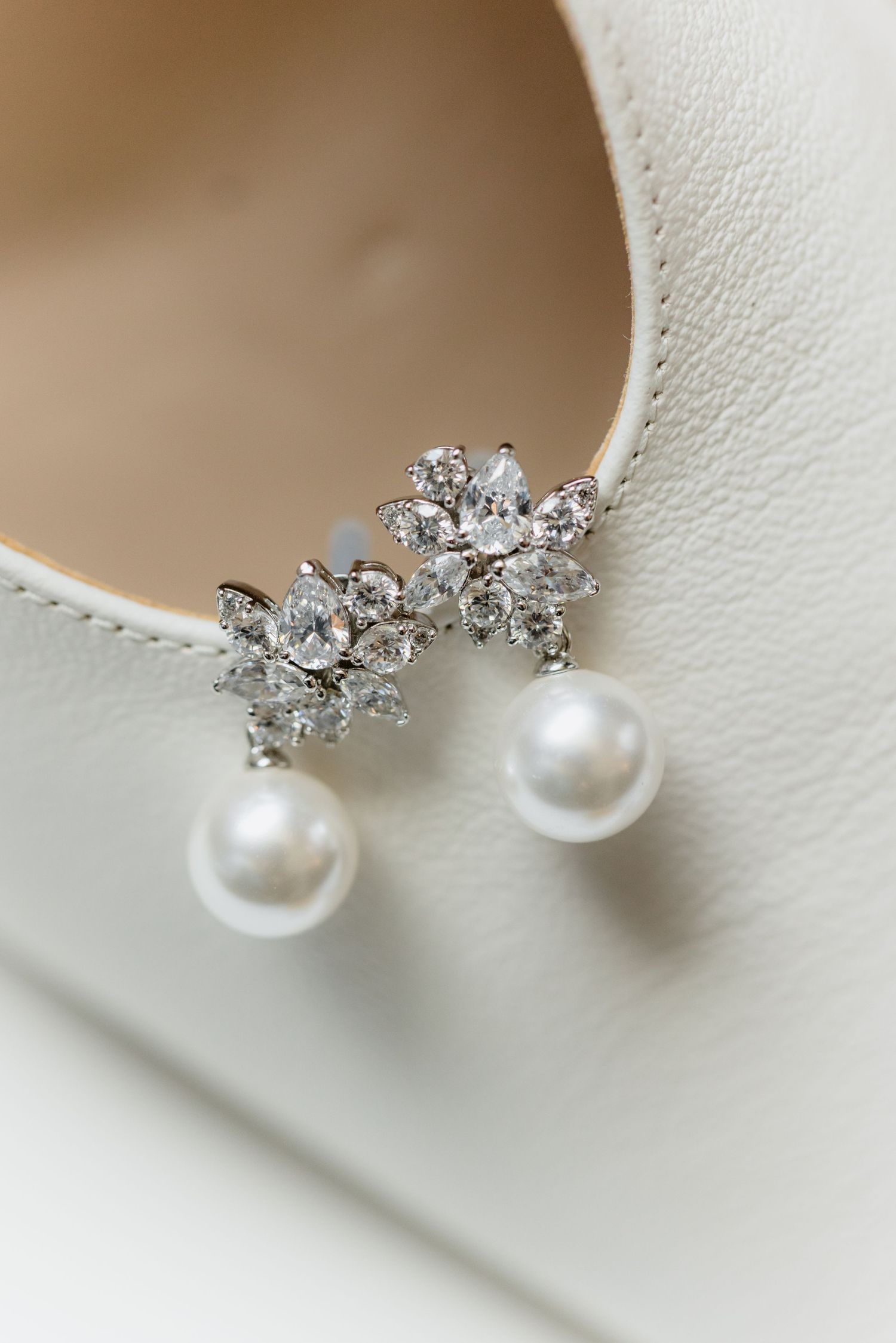 Elegant pearl and crystal drop earrings resting on a white bridal heel shoe.
