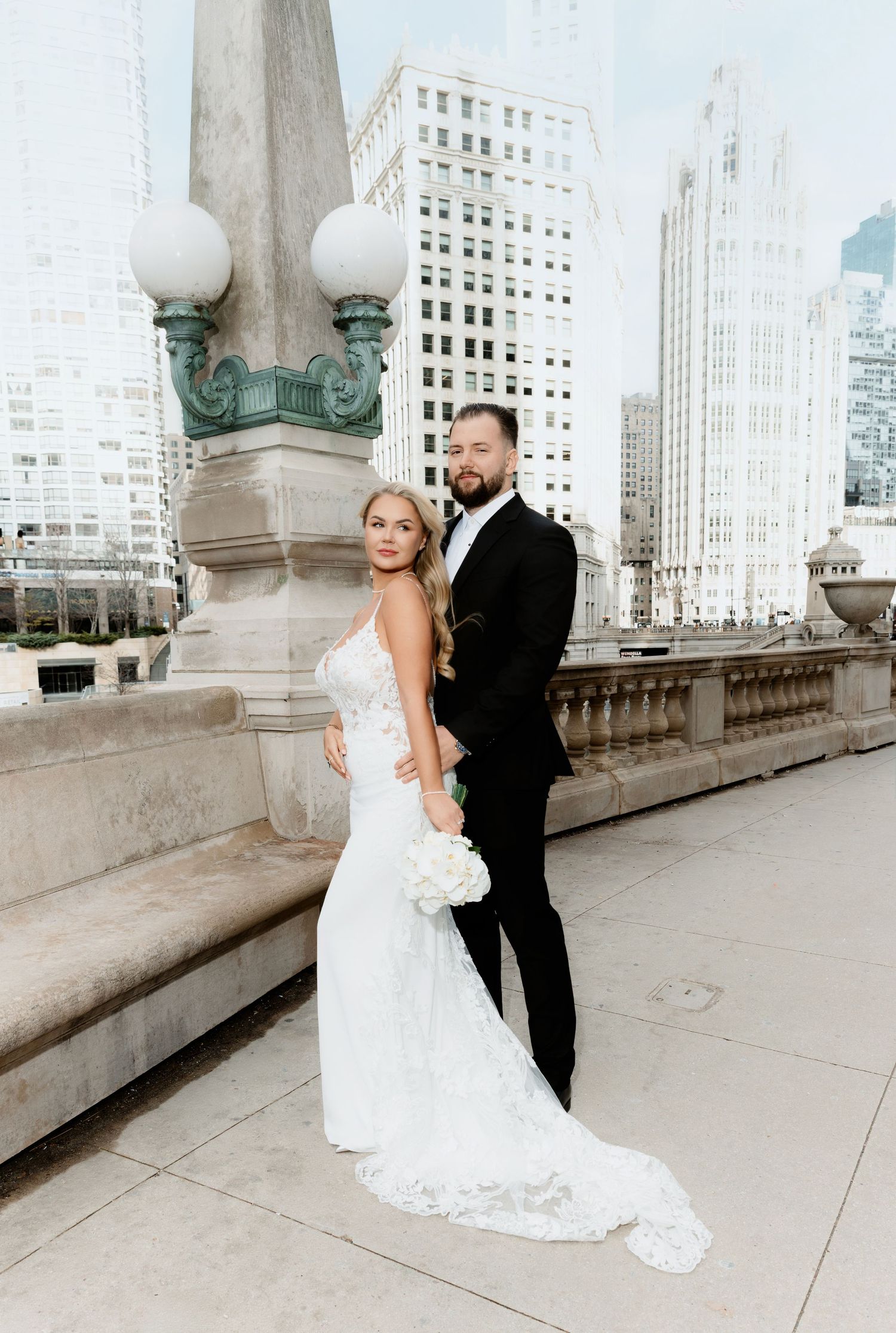 Bride and groom posing elegantly on a Chicago bridge with city skyscrapers in the background.