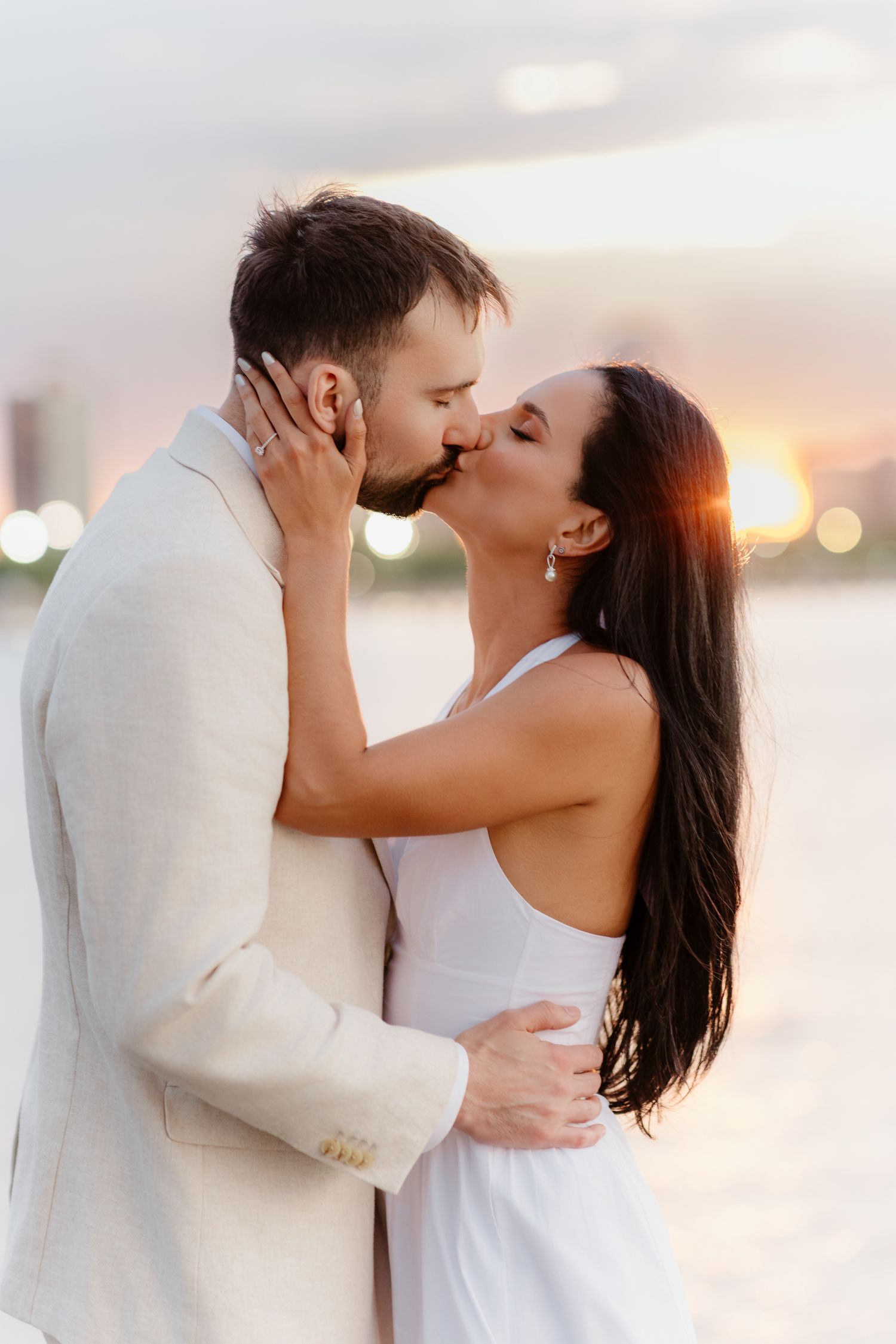 Bride and groom share a passionate kiss at golden hour by the waterfront.