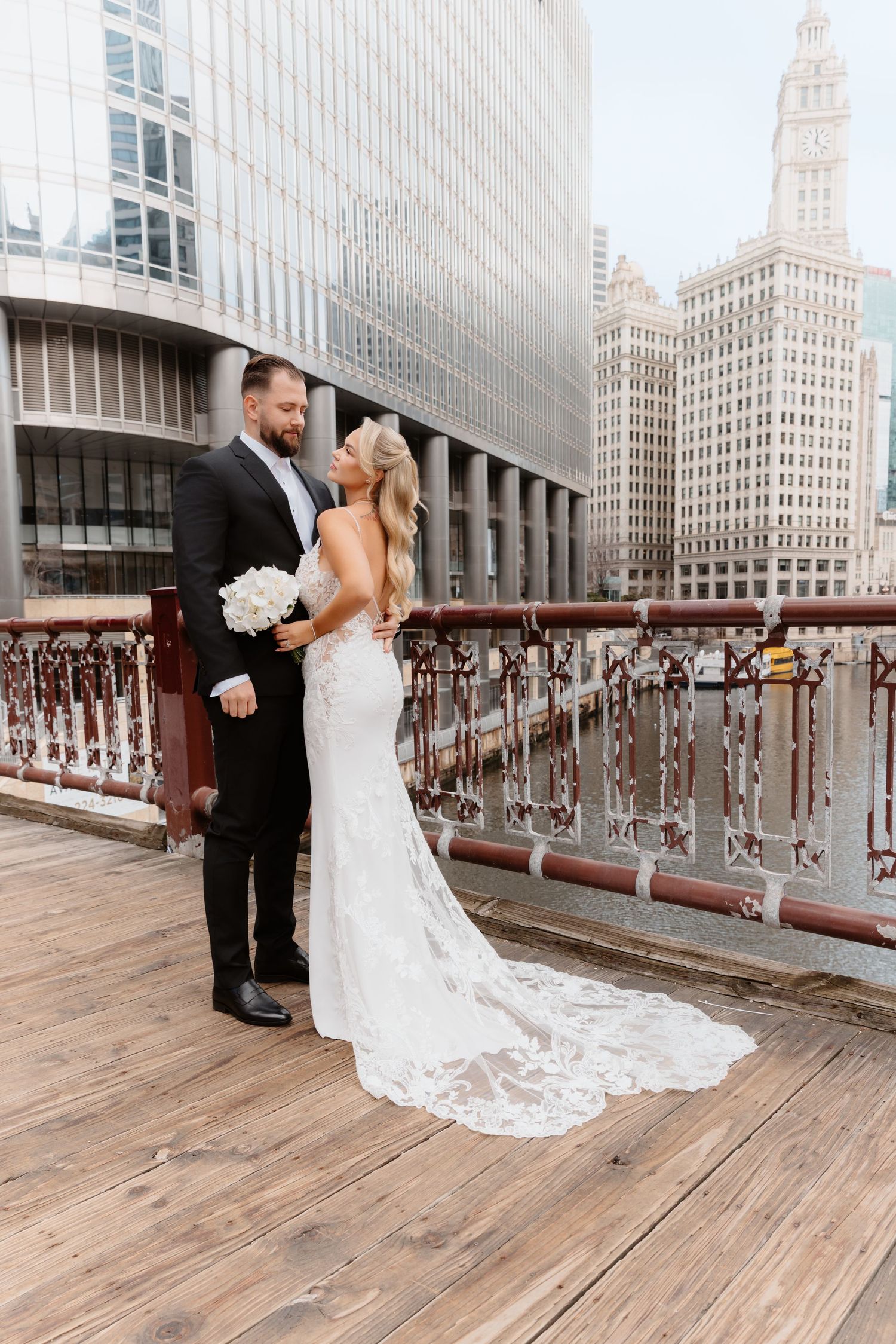 Bride and groom share romantic moment on Chicago riverwalk bridge with city skyline backdrop.