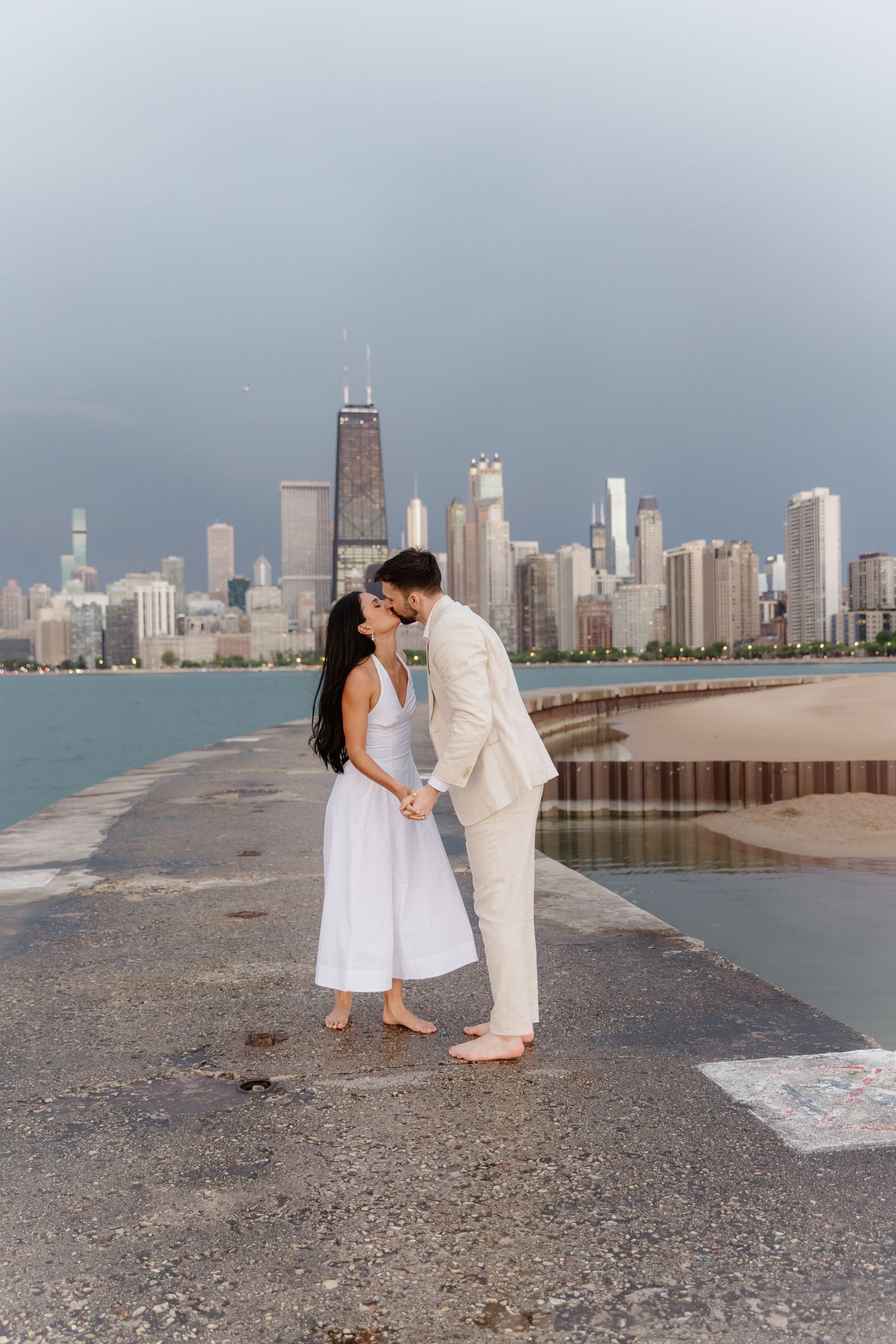 Barefoot couple kissing on pier with Chicago city skyline in the background.