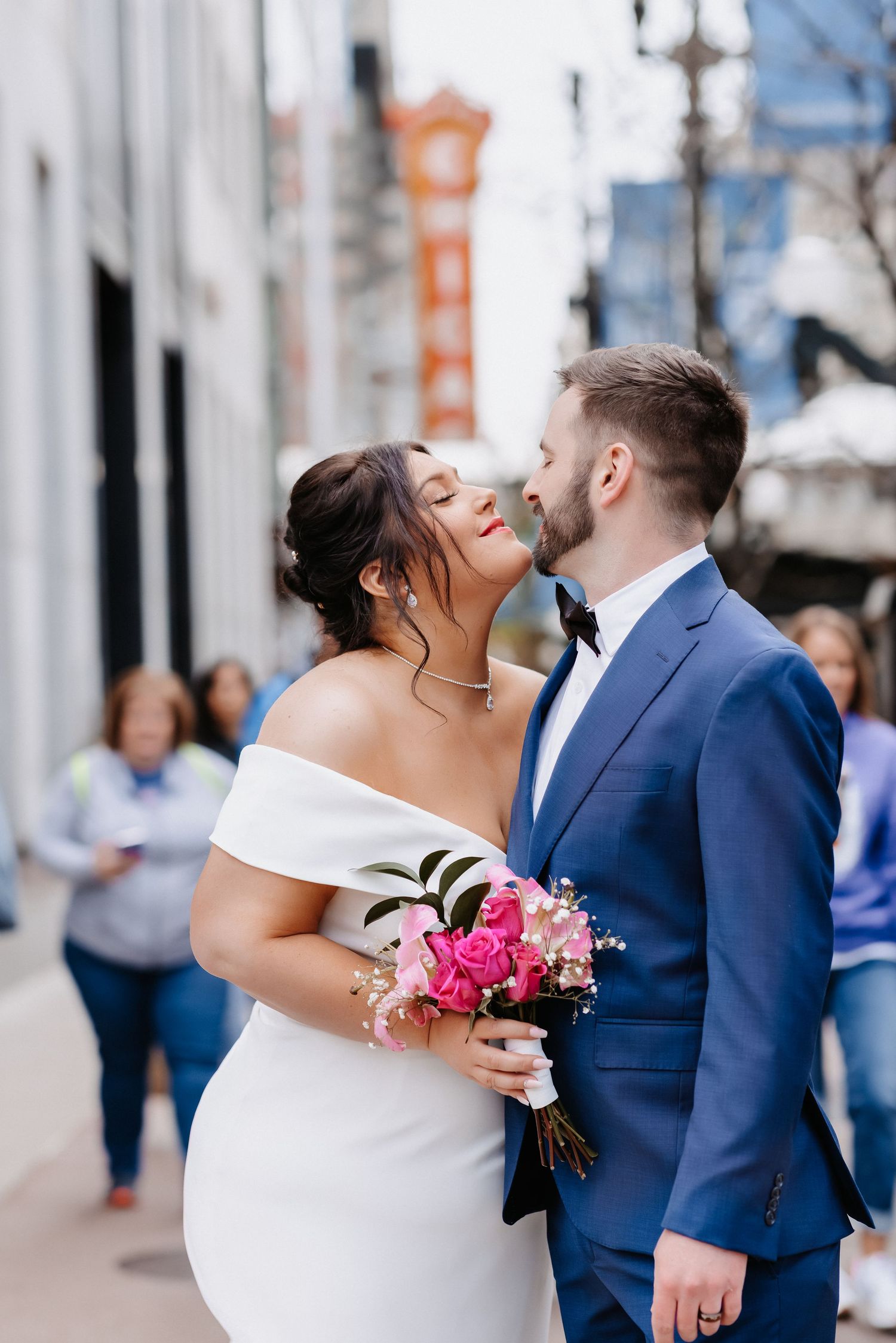 Bride and groom share a romantic kiss on a Chicago street, bride holding vibrant pink rose bouquet.