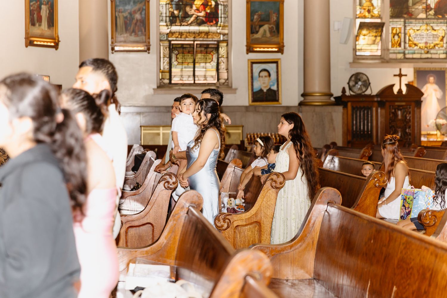 Wedding ceremony in a ornate church with guests seated in wooden pews and bridal party standing at the altar.
