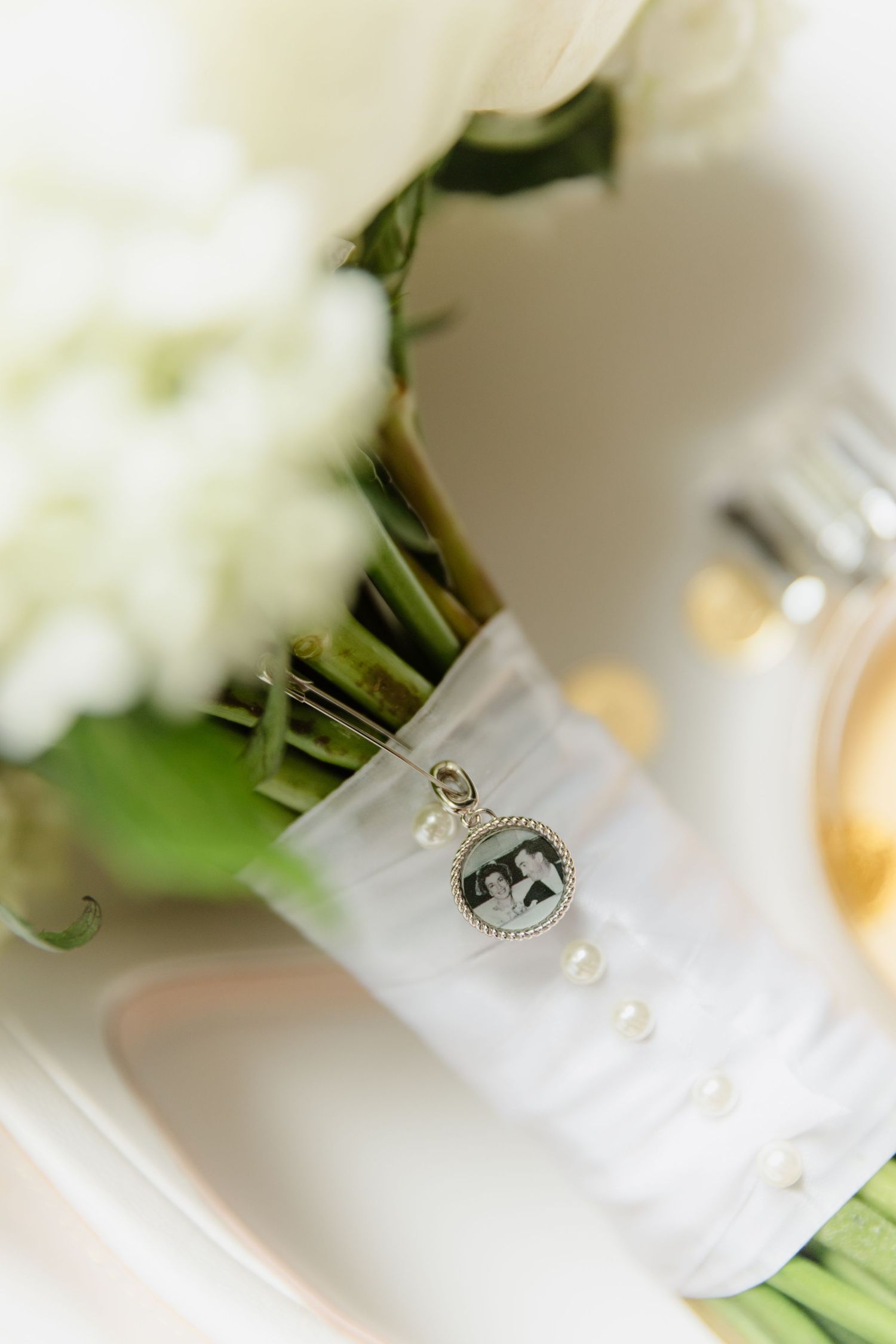 Wedding bouquet with white flowers, satin ribbon, pearl accents, and a vintage photo charm memorial pendant.