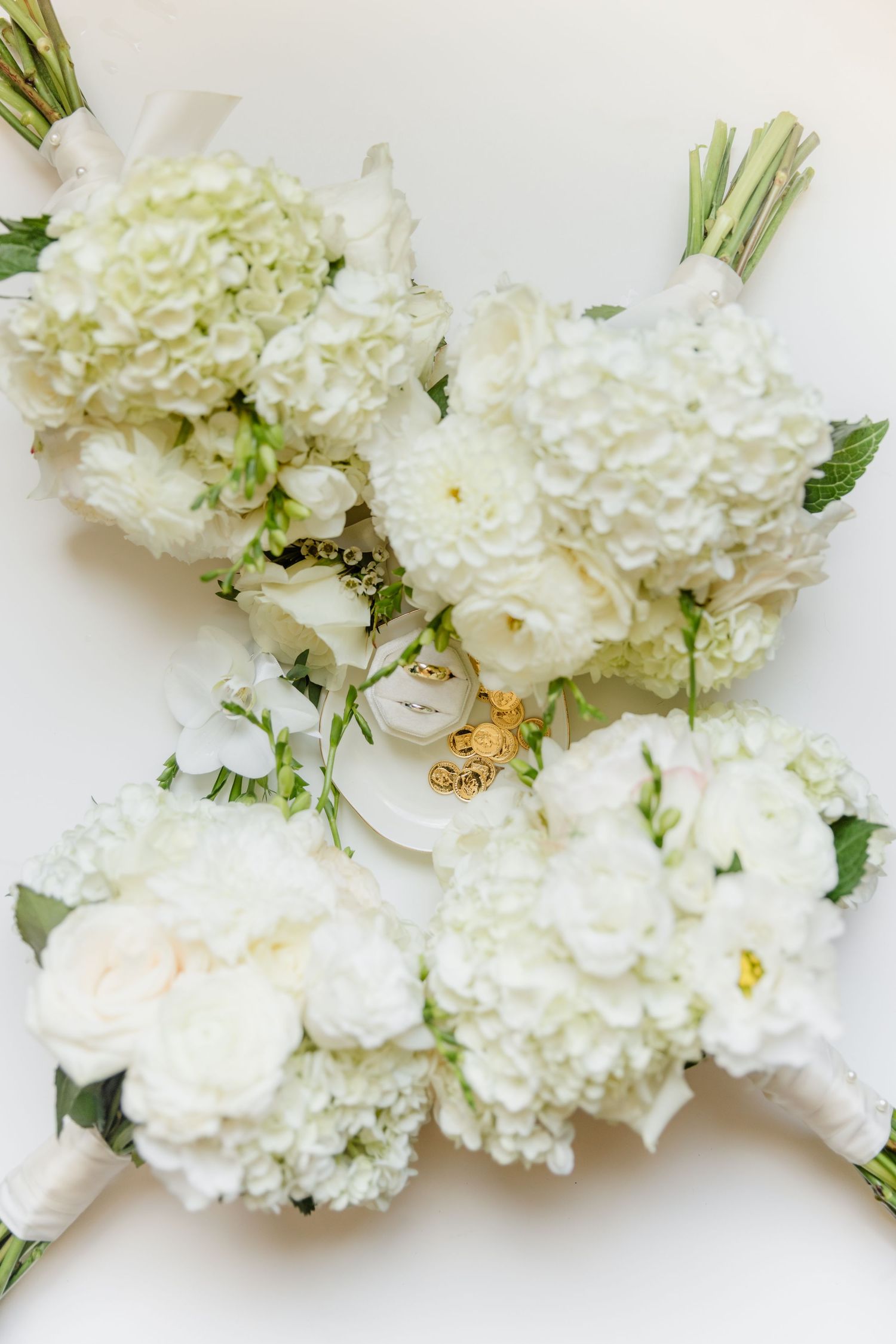 Four matching white wedding bouquets featuring hydrangeas and peonies arranged together with gold earrings.
