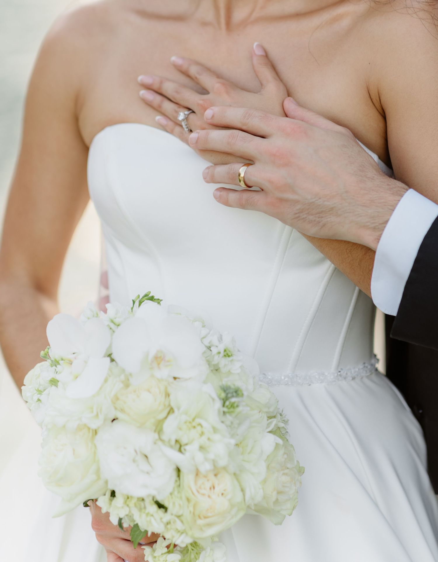 Close-up of bride and groom's wedding rings, bride holding white peony bouquet.