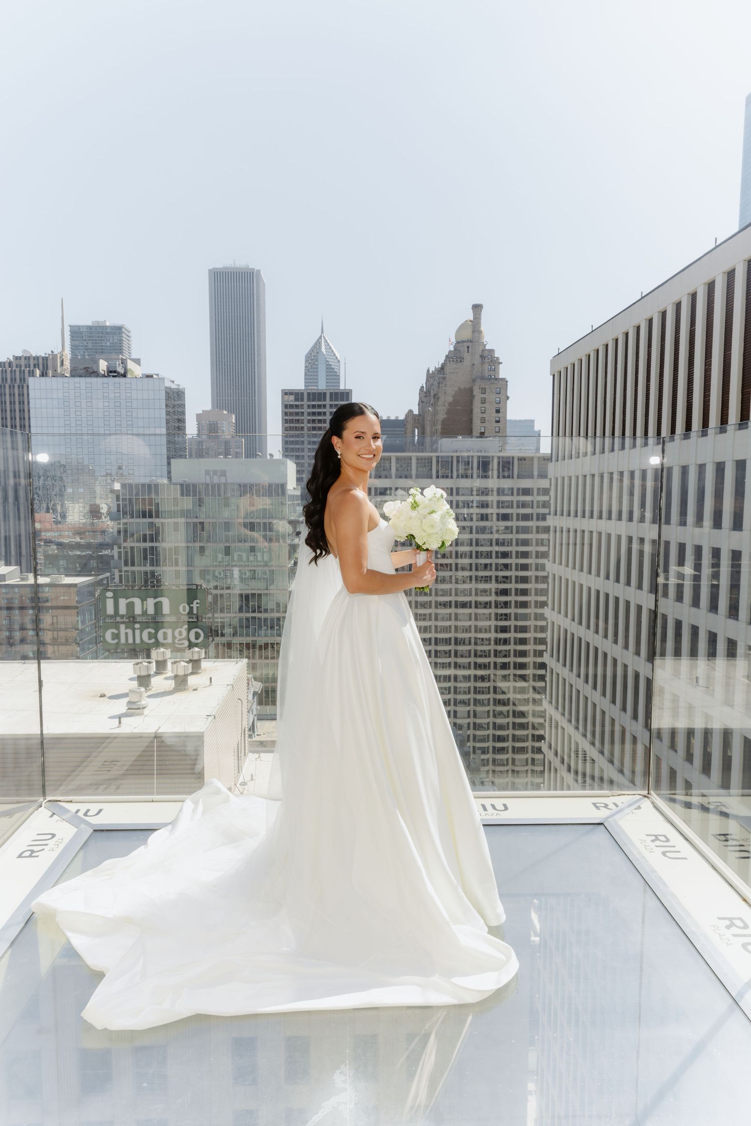 Bride in white strapless gown holding bouquet on rooftop with Chicago skyline backdrop.