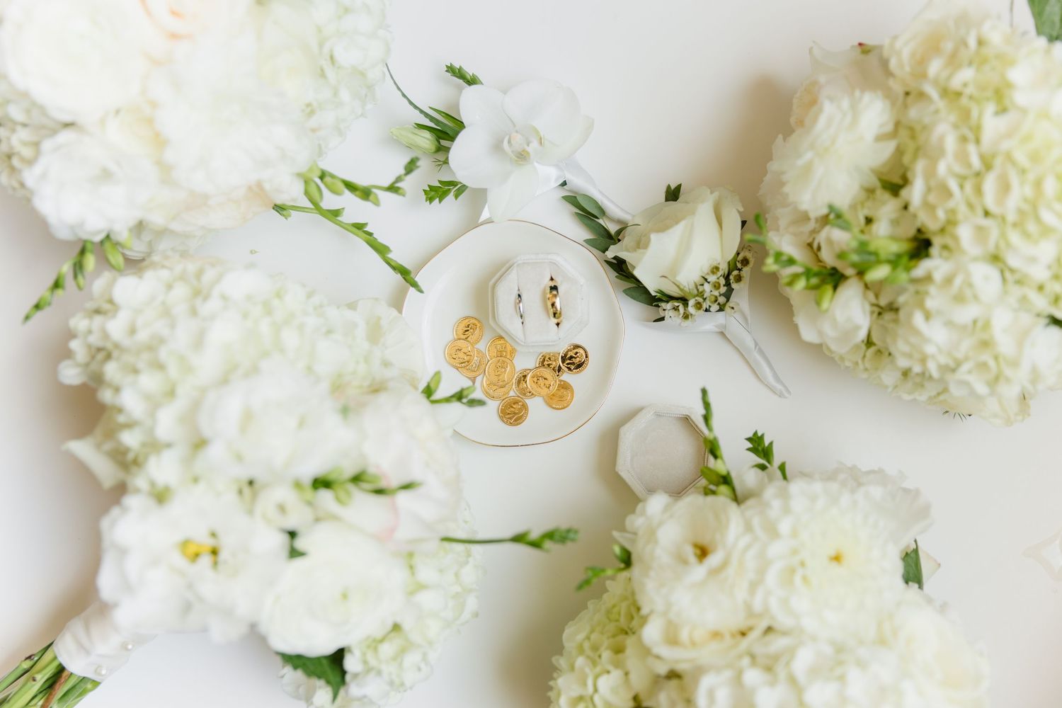 White wedding bouquets surround gold drop earrings on white dish in elegant flat lay.