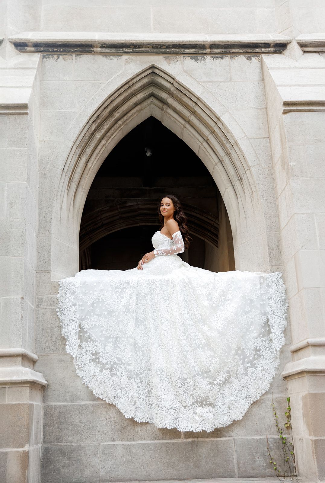 Bride in stunning lace ball gown twirls in Gothic stone archway, dress dramatically fanning outward.