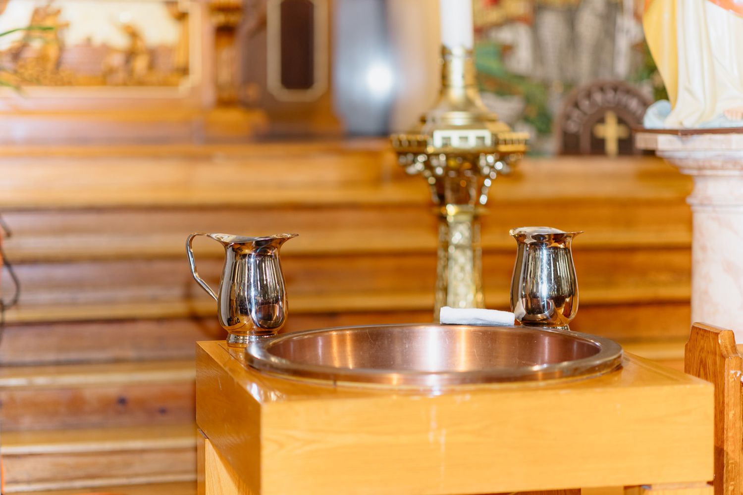 Church baptismal font with silver pitchers and basin on wooden stand near altar.