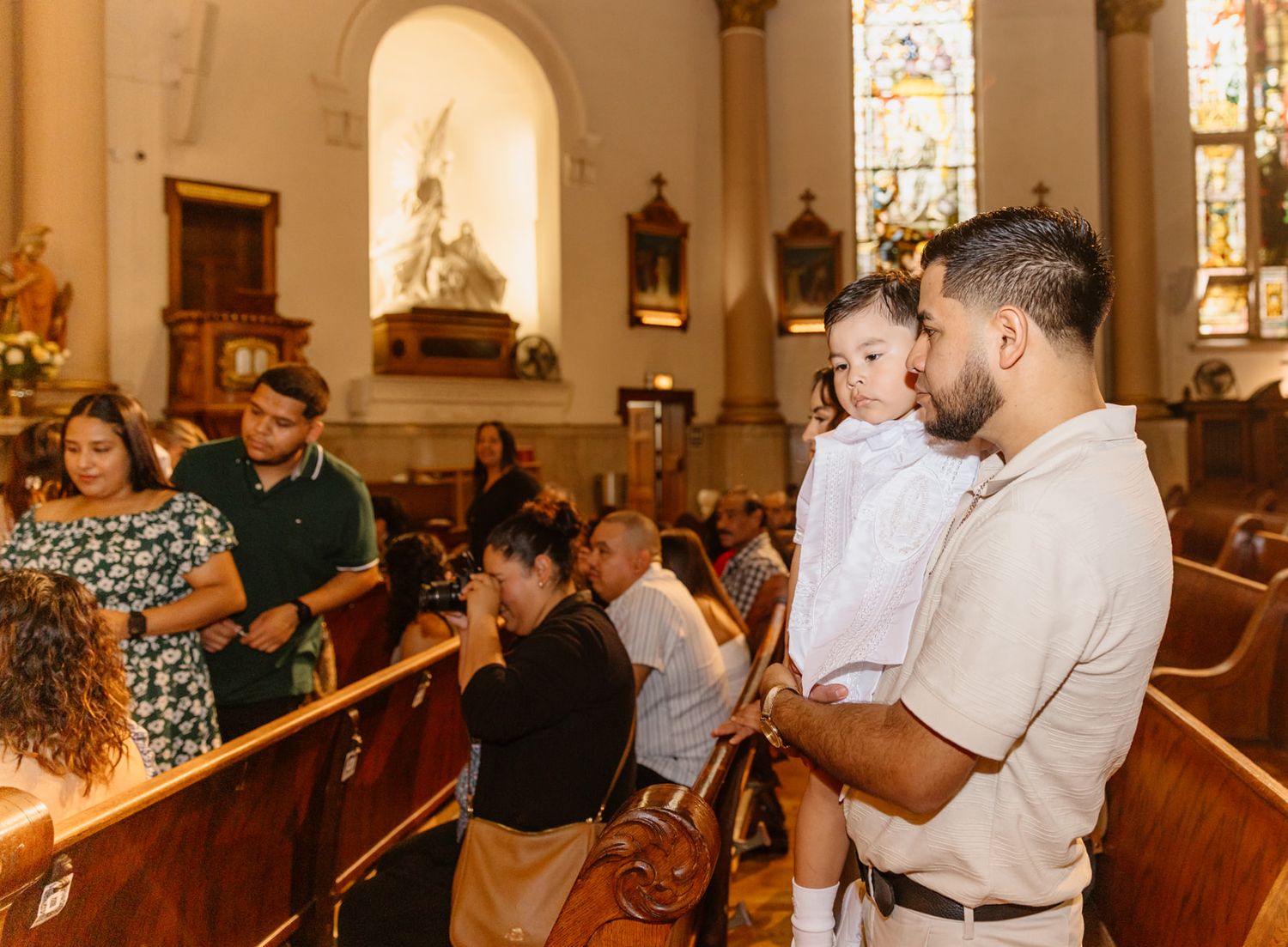 Father holding his baby boy in white baptism outfit inside a Catholic church.