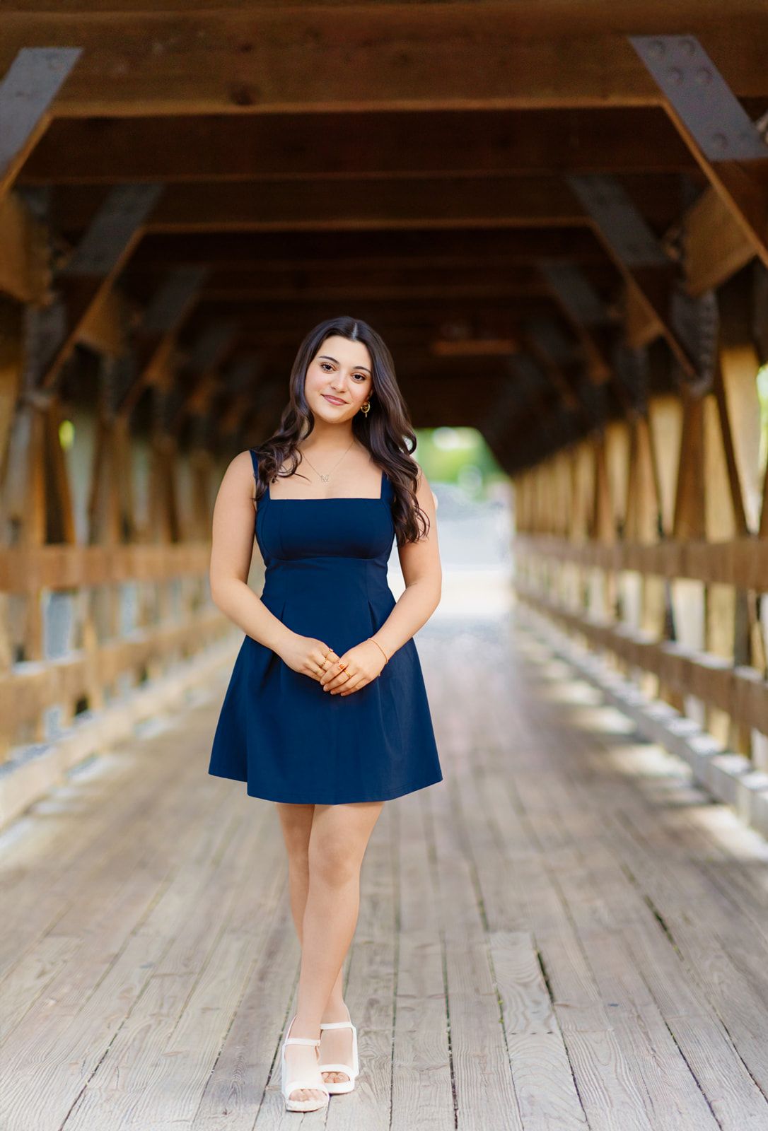 Elegant young woman in navy blue dress posing inside a wooden covered bridge.