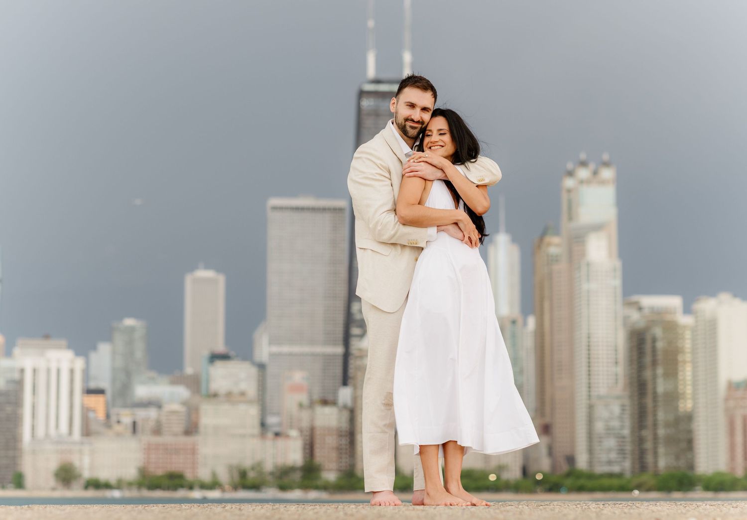 Couple standing together barefoot on Chicago lakefront pier with city skyline visible in the background.
