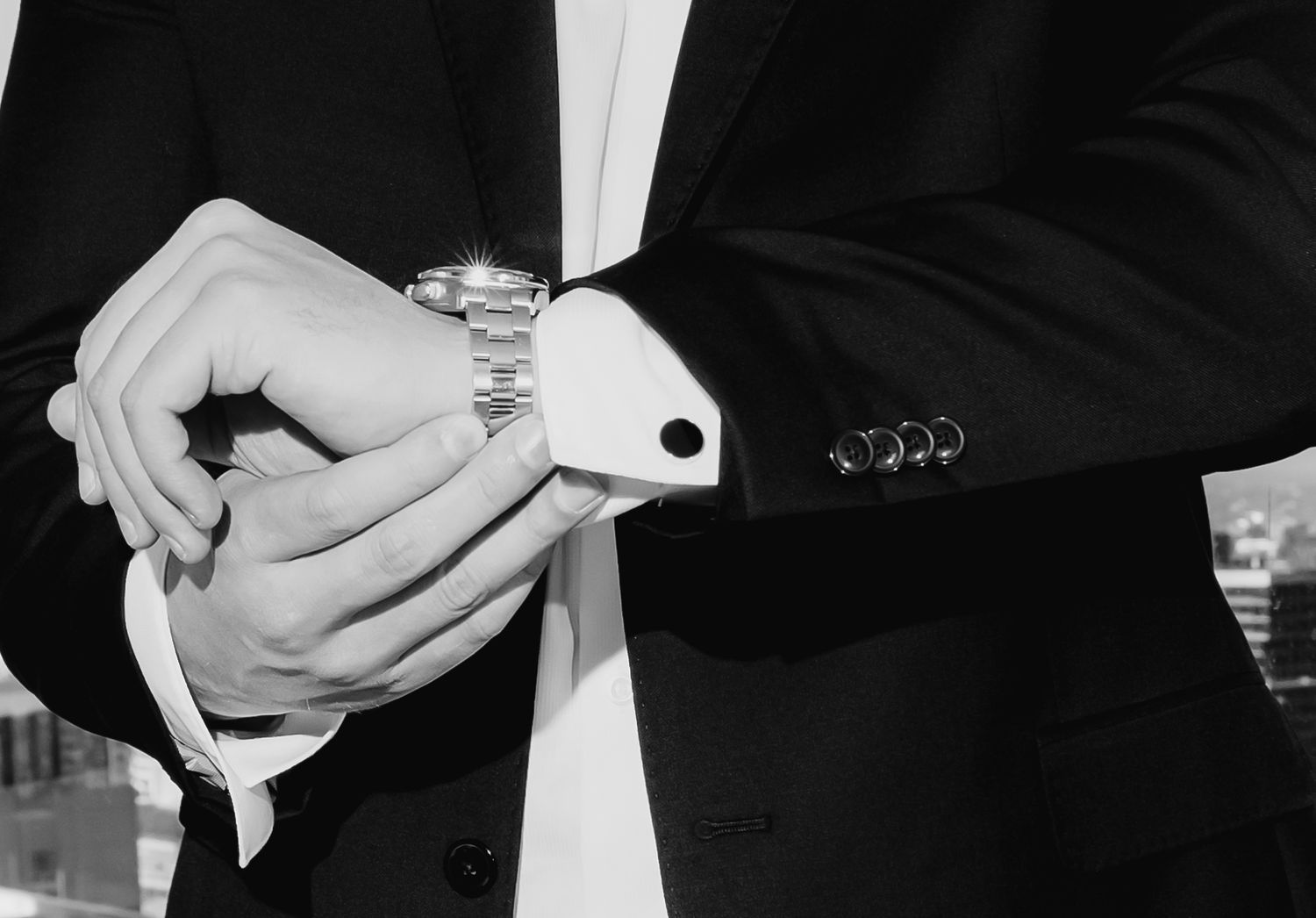 Close-up black and white photo of groom adjusting silver watch and cufflinks on his suit jacket sleeve.