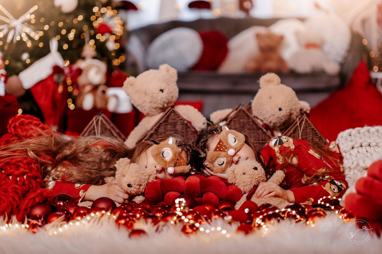 Festive teddy bears surrounded by red Christmas ornaments and glowing lights in holiday decoration.