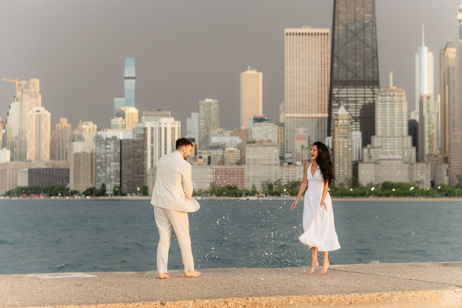 Couple in matching white outfits laughing and splashing water by Chicago lakeshore.