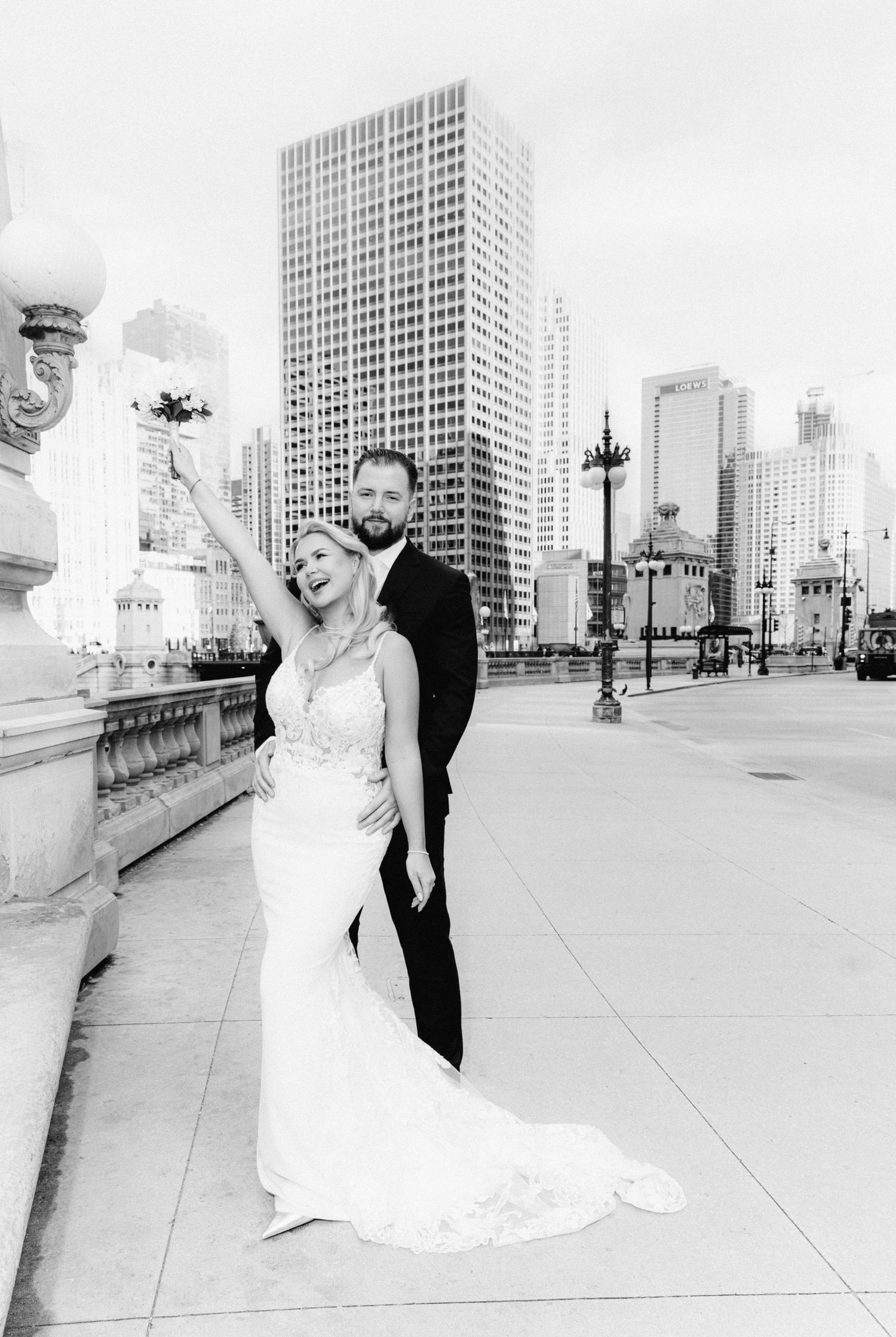 Bride and groom pose on Chicago bridge with city skyline in black and white wedding photo.