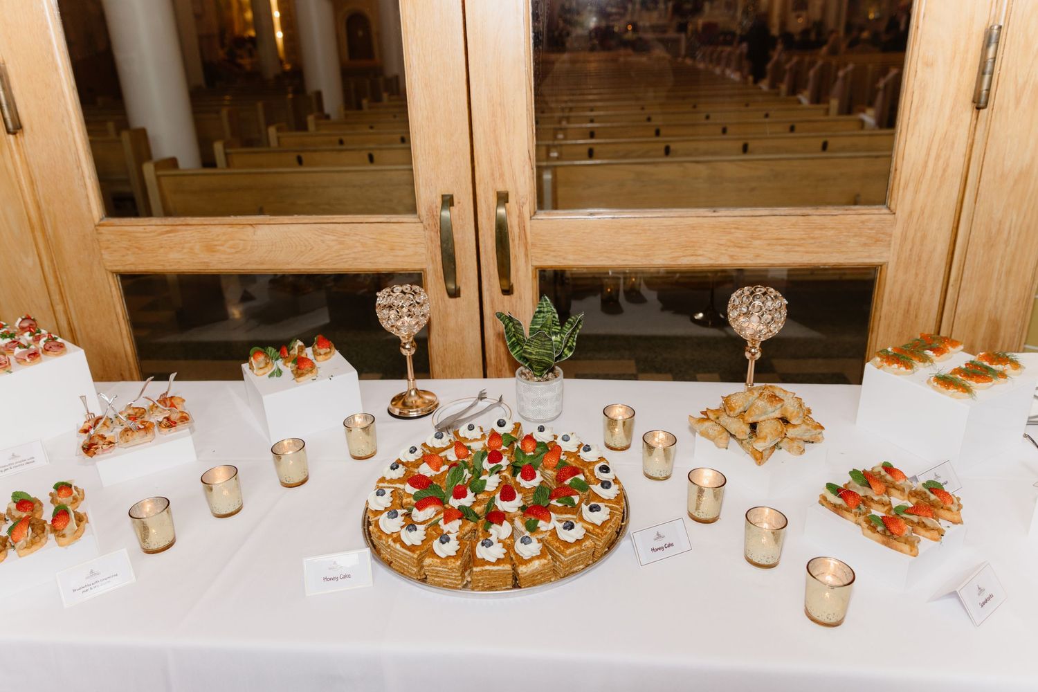 Elegant wedding reception appetizer table with canapes, crystal candleholders, and votive candles in a church venue.