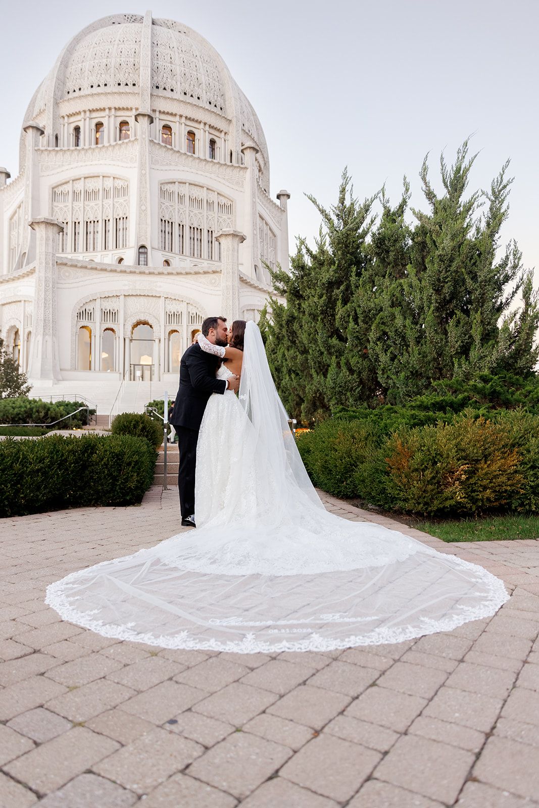 Wedding couple sharing a romantic kiss outside the domed Bahai Temple with an elegant lace cathedral veil.
