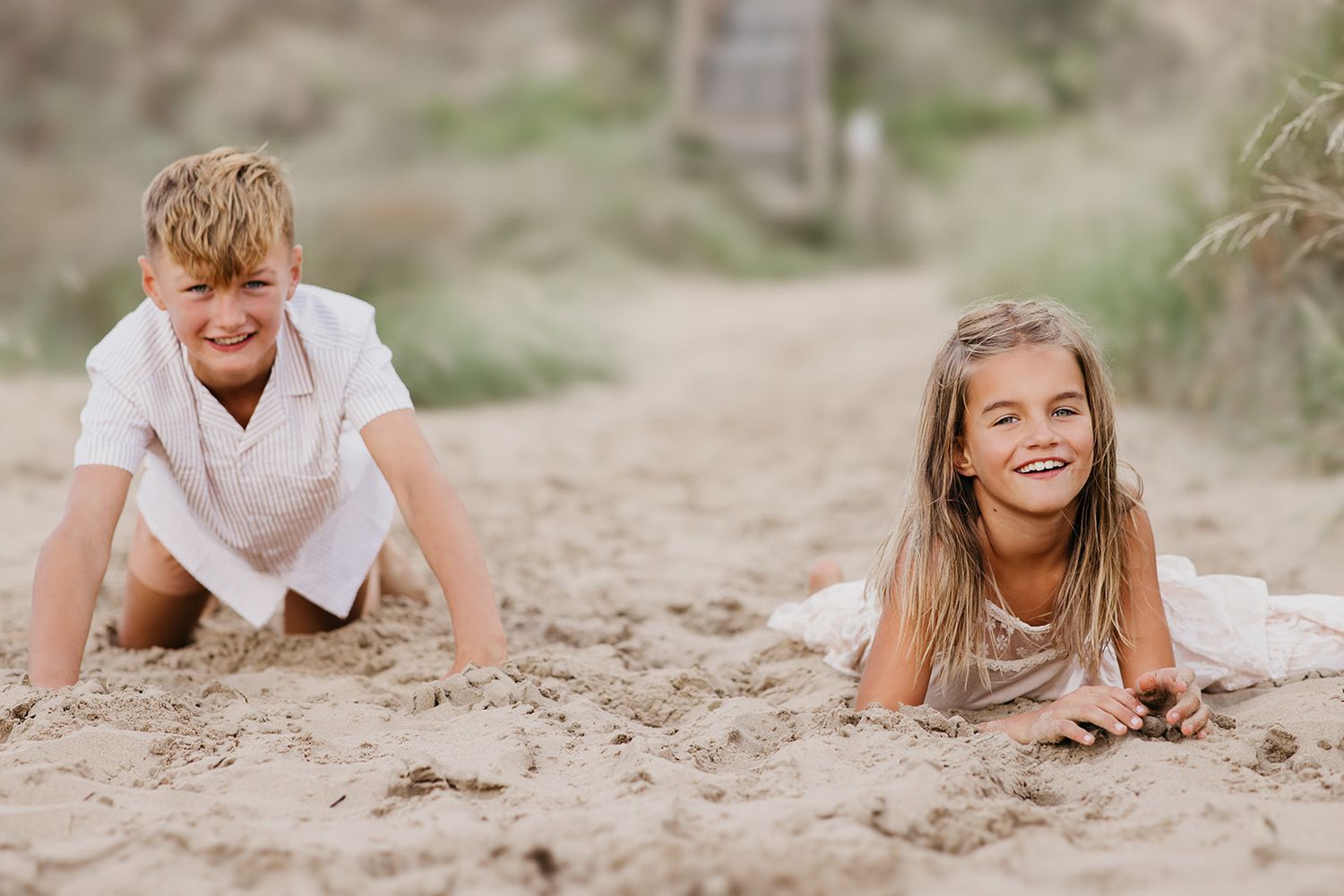 Two happy children playing in the sand at the beach, laughing and lying down on a sunny day.