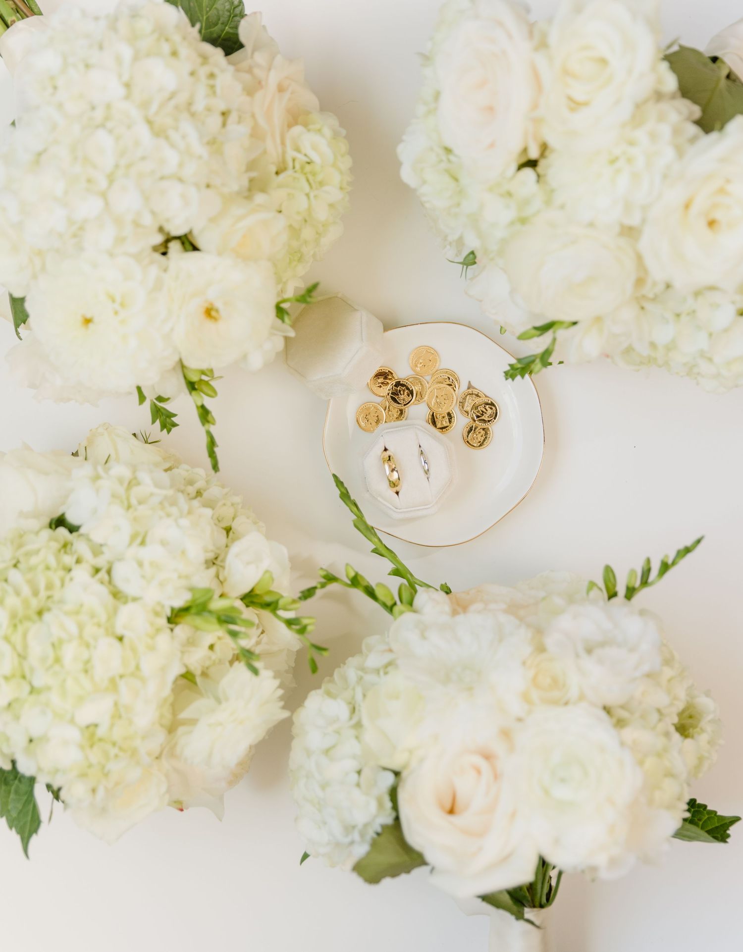 White hydrangea and rose bridal bouquets arranged around a dish with gold earrings and rings.