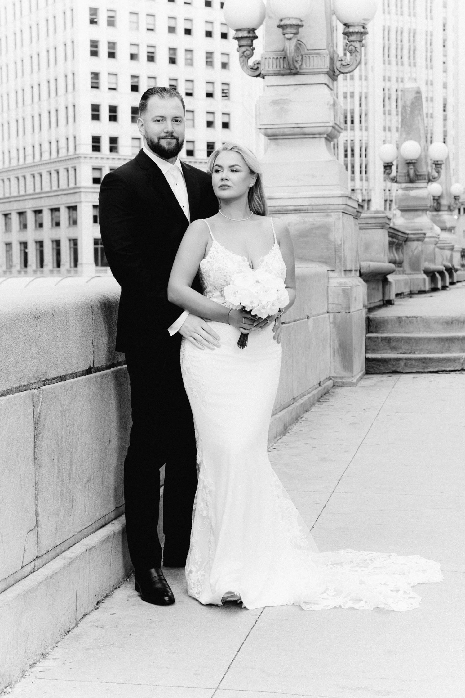 Black and white portrait of bride and groom posing on a Chicago bridge with city buildings behind them.