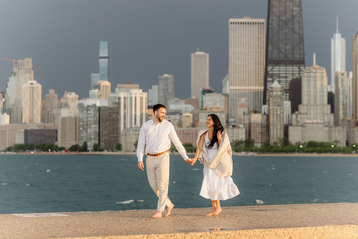 Happy couple walking hand in hand along Chicago lakefront with stunning city skyline in the background.