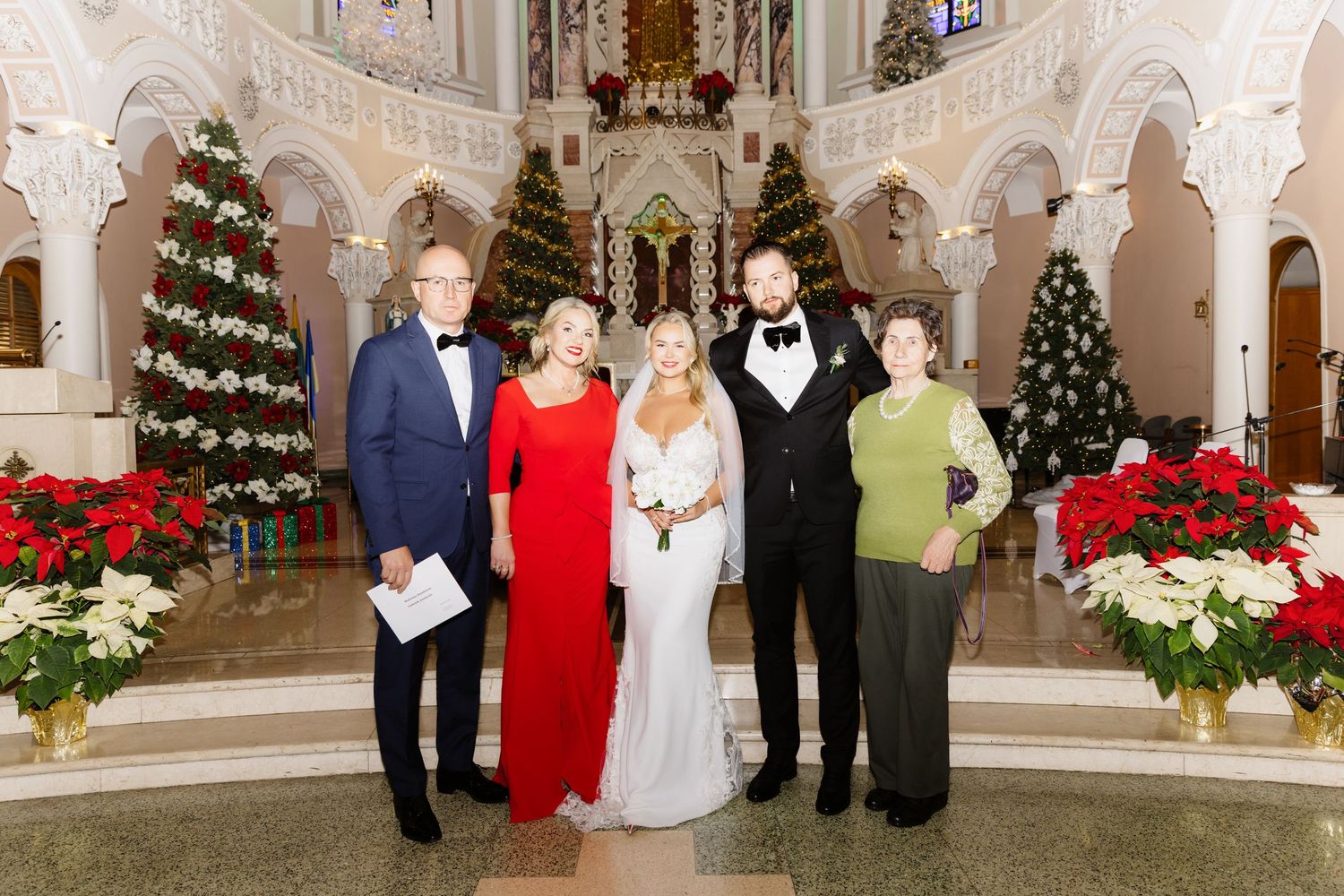 Newlyweds and family members smiling together in an ornate church beautifully decorated with Christmas trees and poinsettias.