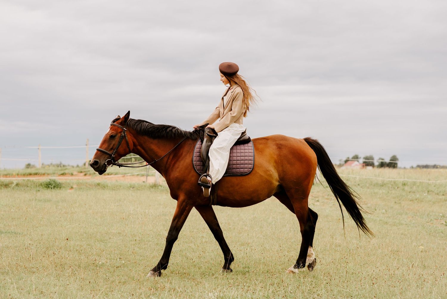 Young woman riding a chestnut horse bareback across an open grassy field.