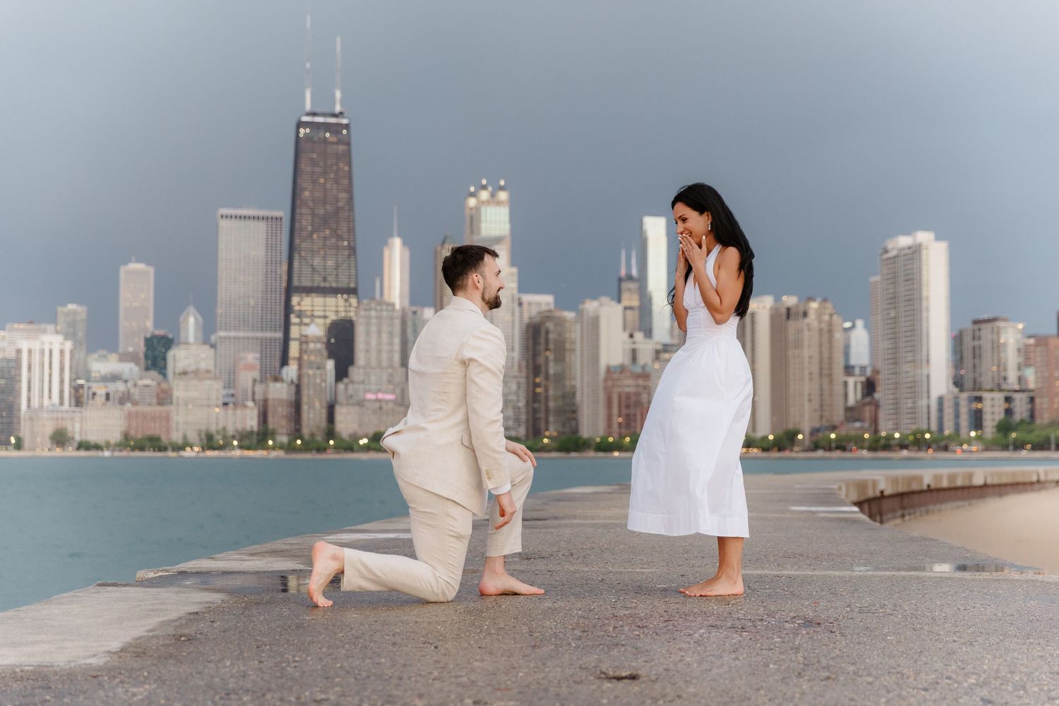 Man proposing on one knee to woman with Chicago skyline in background.