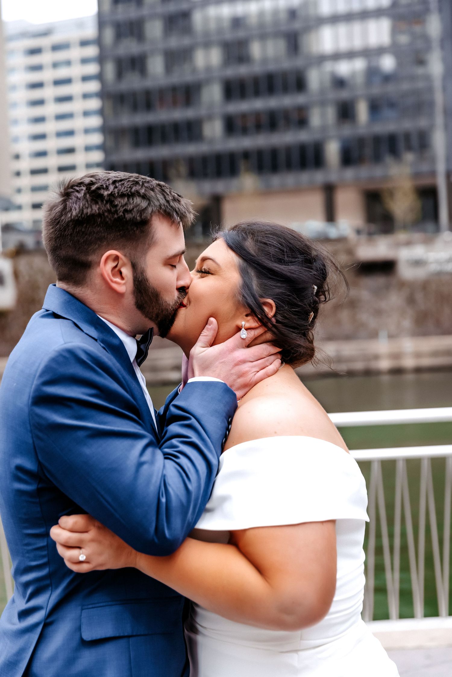 Newlyweds share romantic first kiss with groom in blue suit beside Chicago River after ceremony.