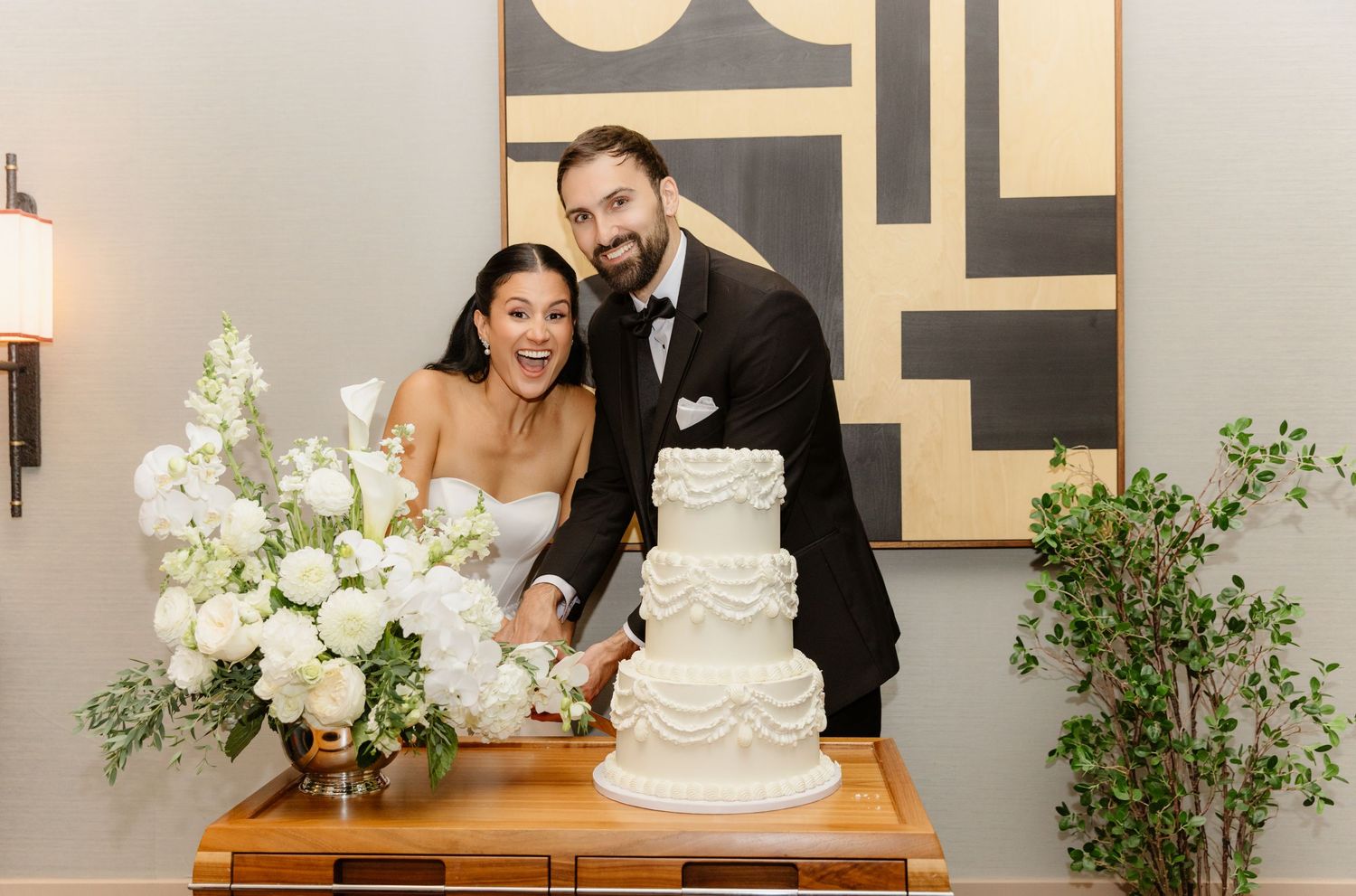 Smiling bride and groom cutting a white tiered wedding cake at their elegant reception.