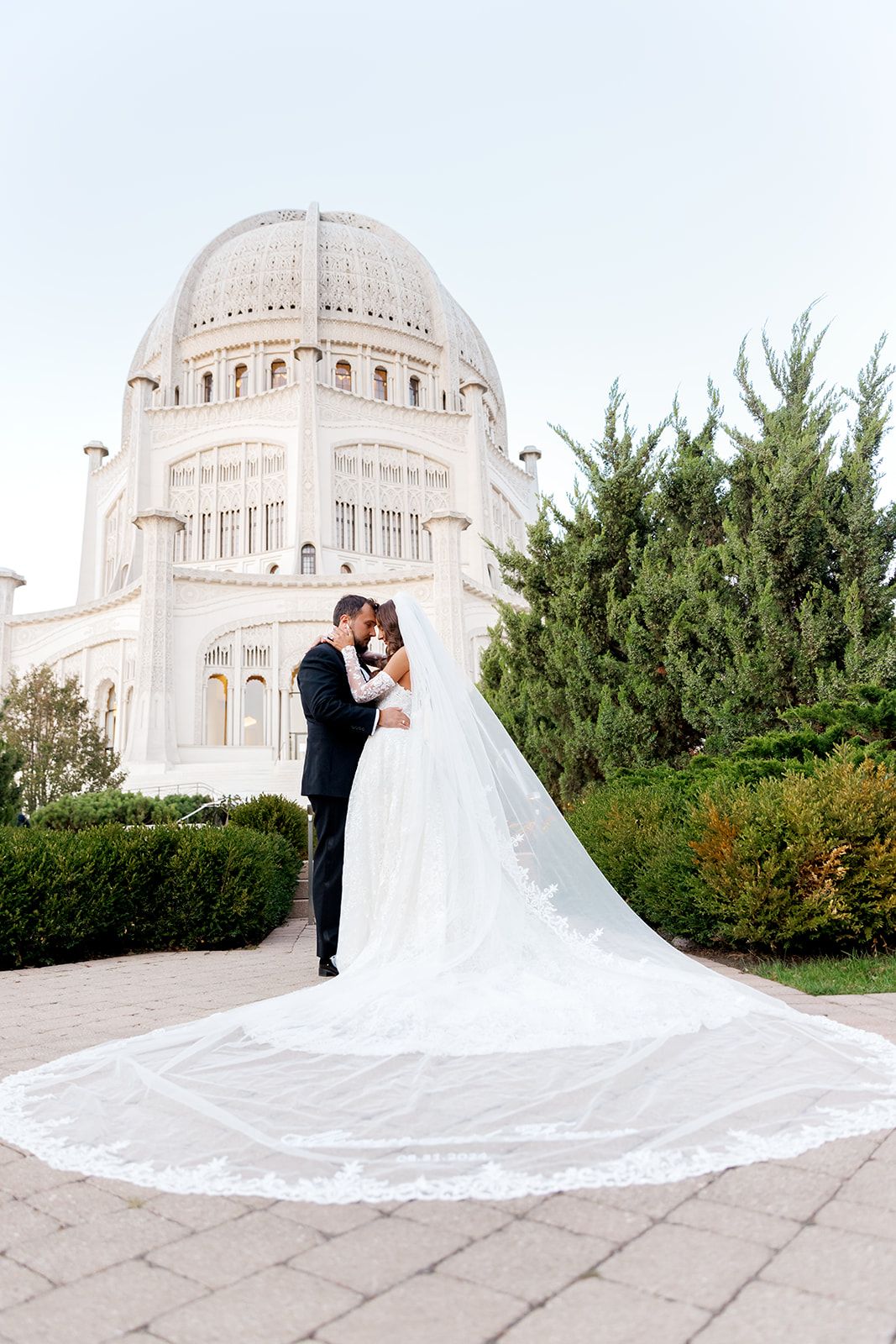 Bride and groom kiss before the Bahai Temple as her cathedral lace veil fans across the ground.