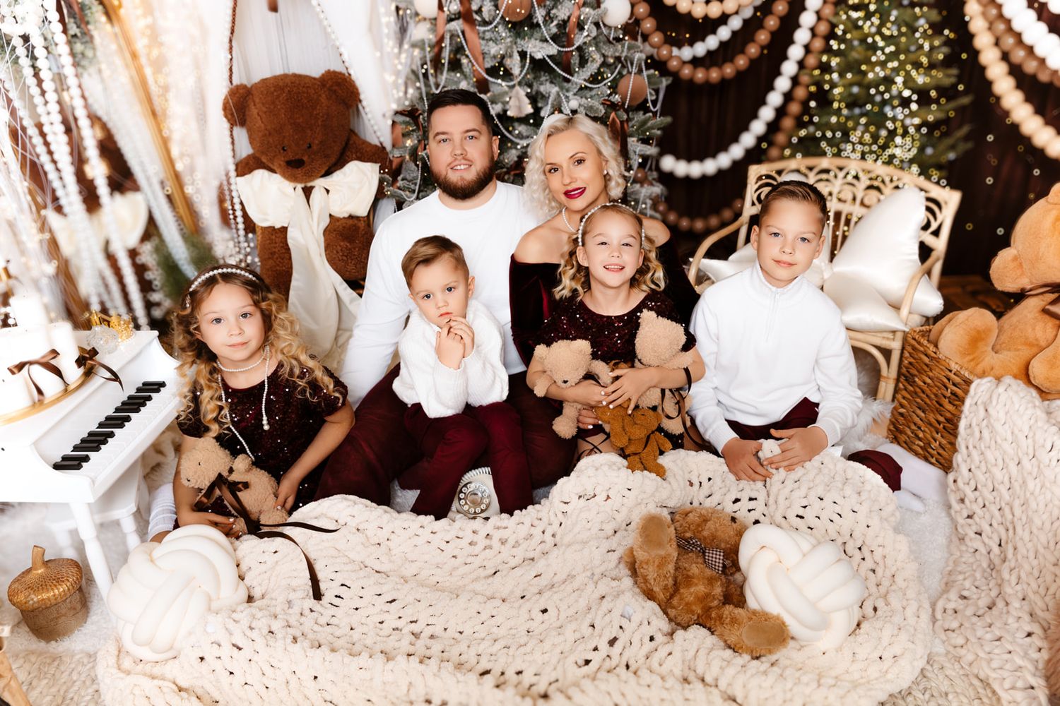 Family of six poses together for a festive Christmas photo with teddy bears and holiday decorations.