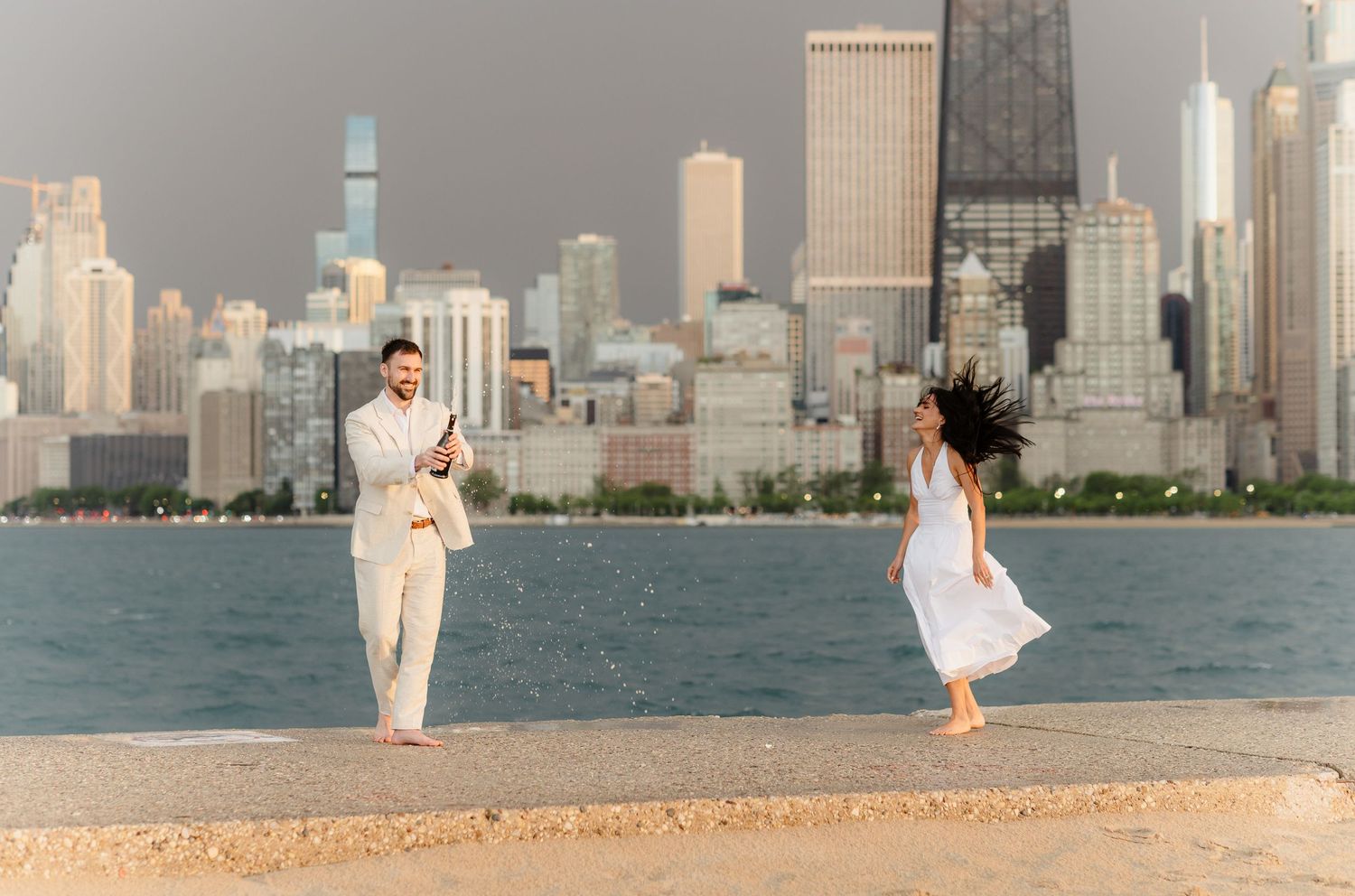 Man photographing woman twirling in white dress on Chicago lakefront with city skyline.