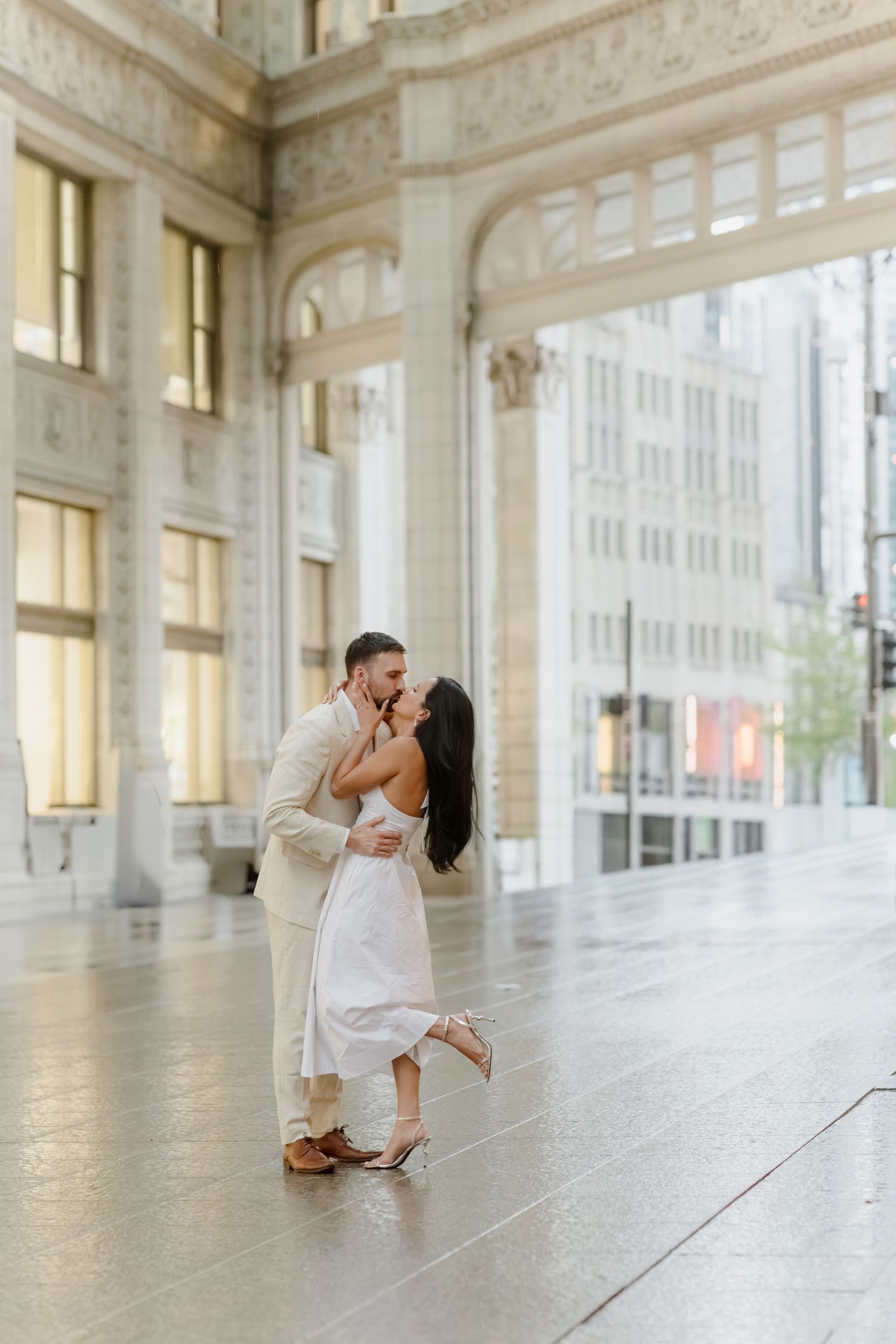 Couple sharing passionate kiss inside grand white marble architectural arcade at sunset.