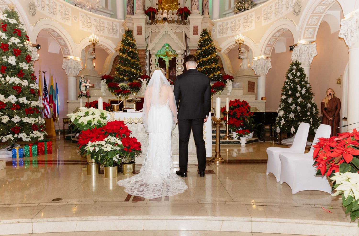 Bride and groom at church altar flanked by Christmas trees and red poinsettia floral arrangements.